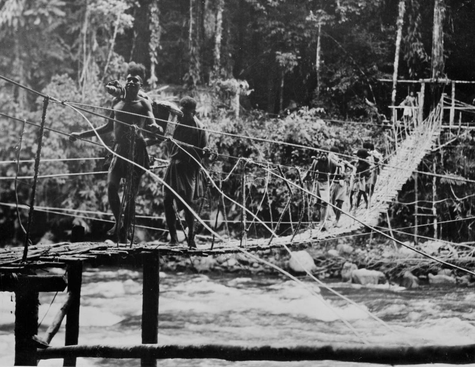 Men carry supplies over a newly built bridge.