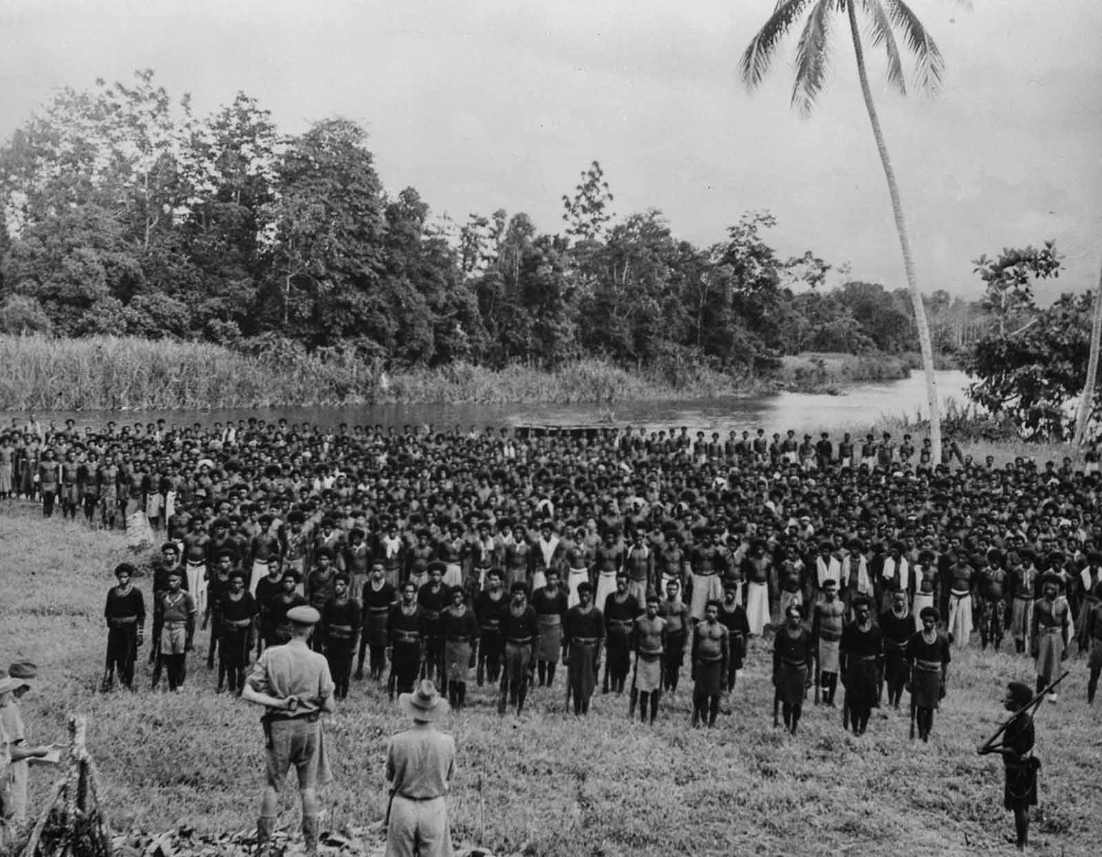 Hundreds of New Guinean stretcher and supply carriers stand at attention as Australian Major General George Alan Vasey thanks them in a medal ceremony.