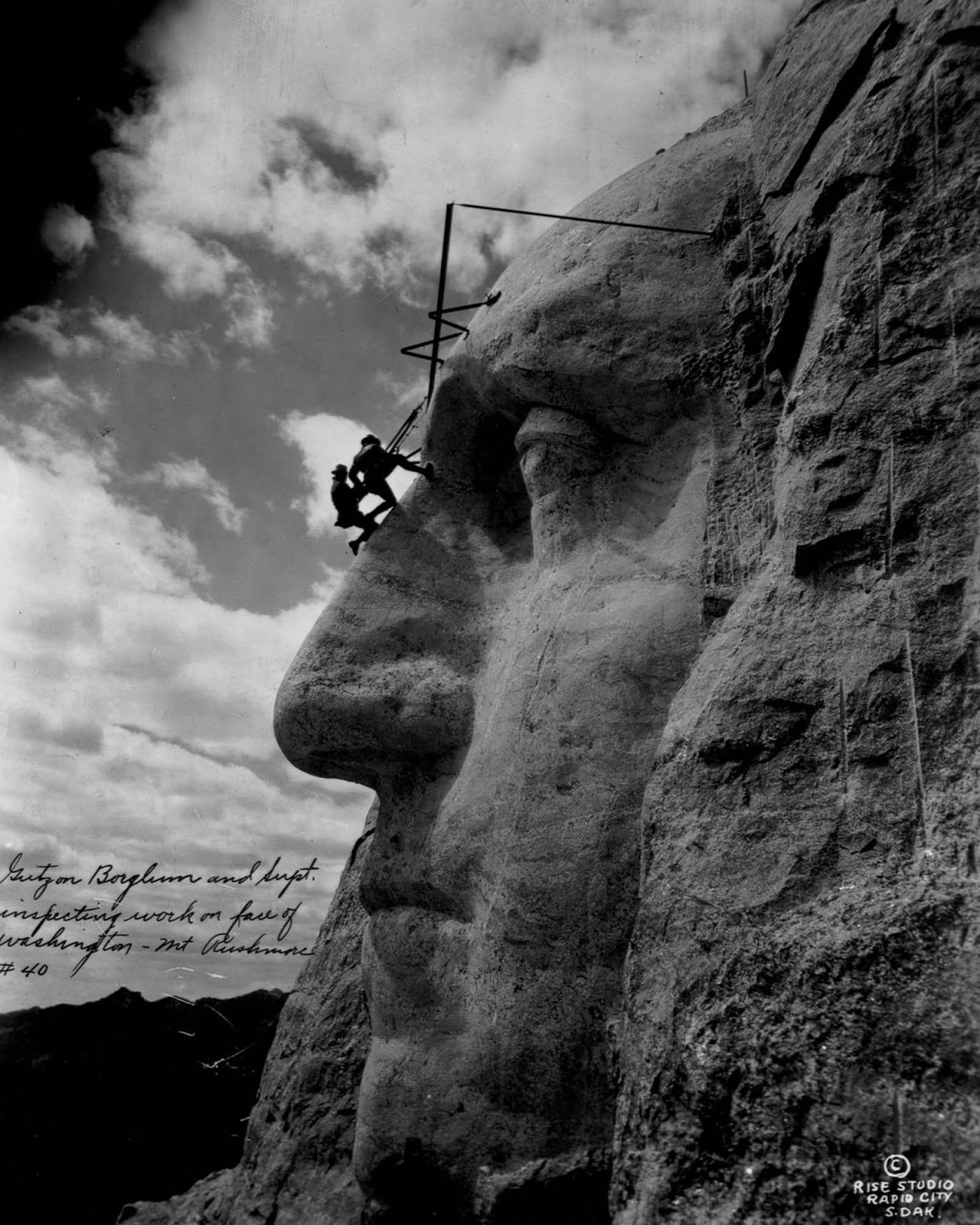 Gutzon Borglum and another sculptor hang from the forehead of George Washington. 1932.