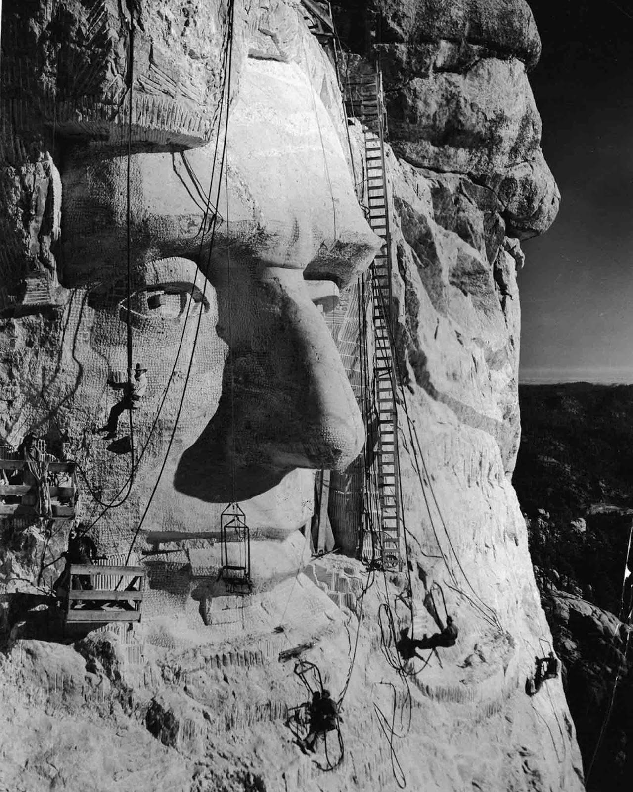 Gutzon Borglum hangs below an eye as his crew works on Abraham Lincoln's head. 1935.