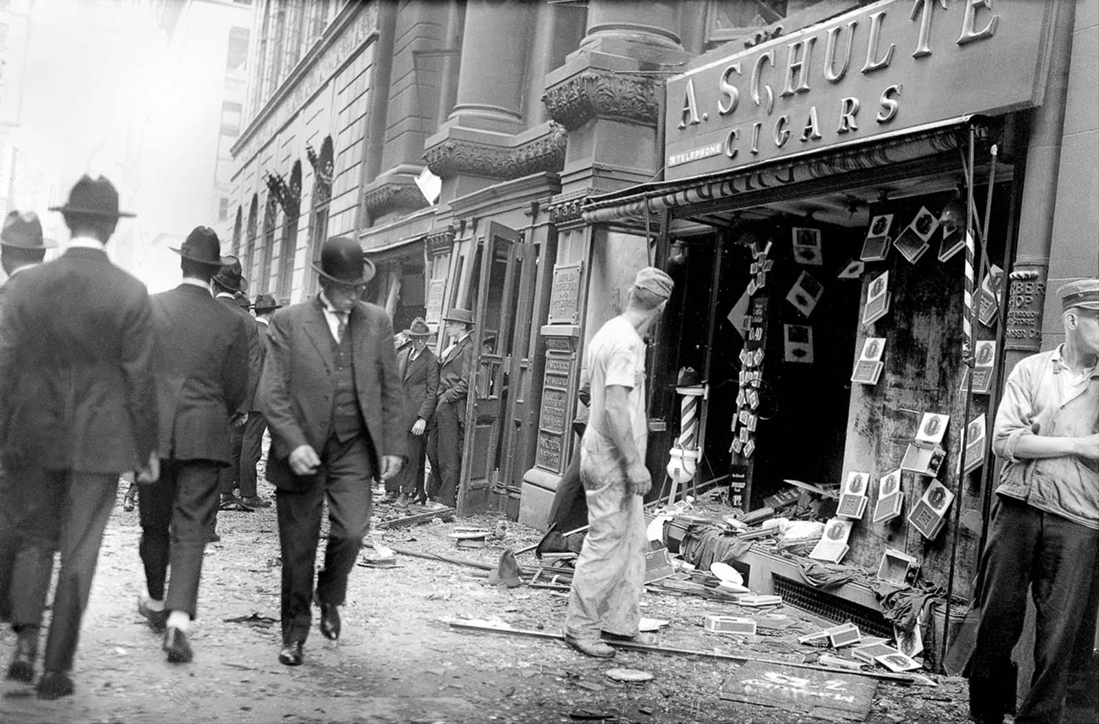 Bystanders walk by the wrecked facade of a cigar store.
