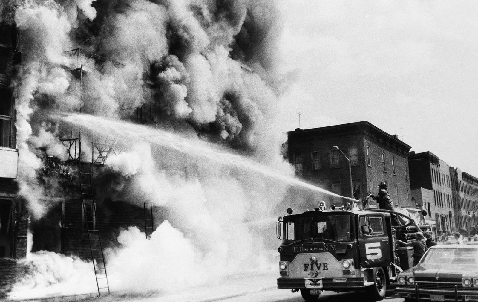 Firemen fight a blaze above a row of looted stores in New York's Brooklyn borough, July 14, 1977, the day after the power failure. The stores were looted during blackout.