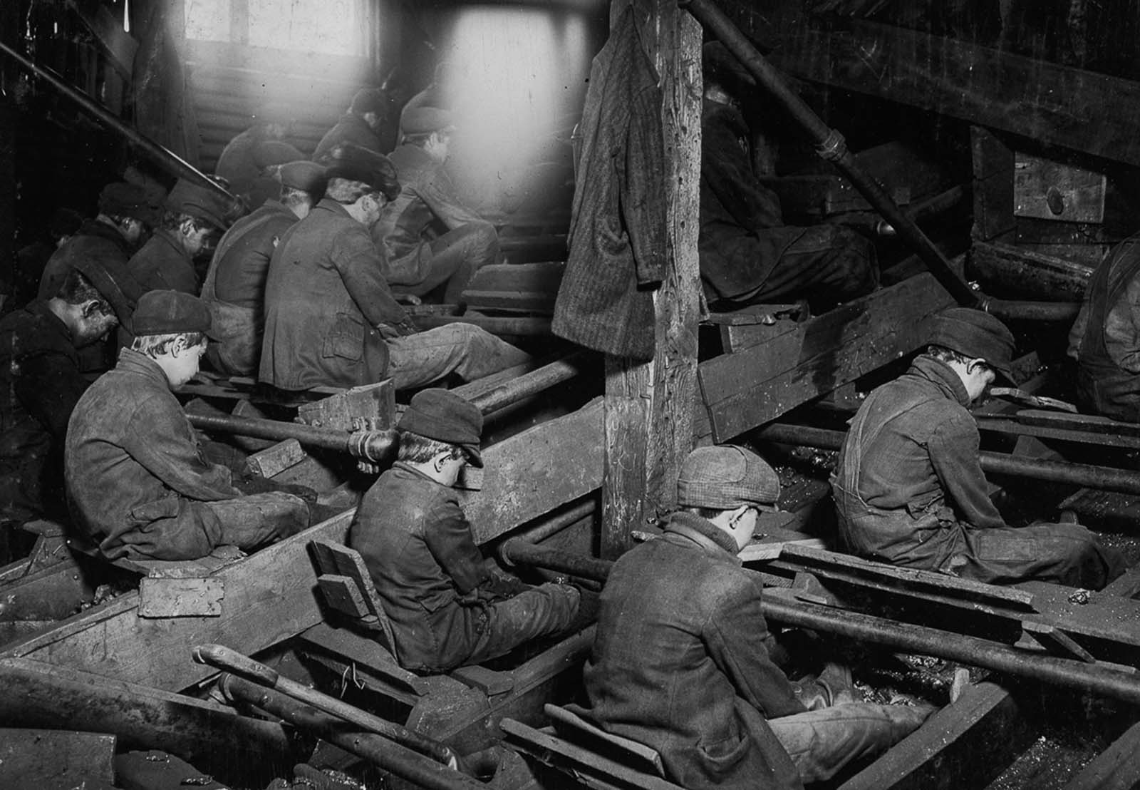 Breaker boys at work breaking coal. The process produces clouds of dust which coat the workers' lungs. 1911.