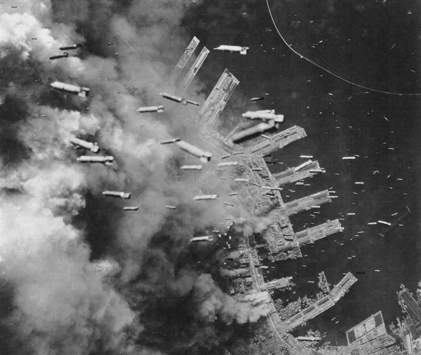 Incendiary bombs are dropped from B-29 Superfortresses of the U.S. Army Air Forces on already-burning landing piers and surrounding buildings in Kobe, Japan, on June 4, 1945.