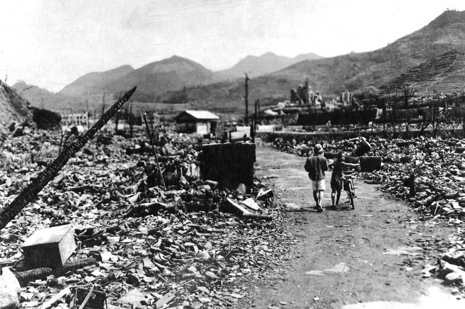 People walk through the charred ruins of Nagasaki, shortly after an atomic bomb destroyed much of the city. The explosion generated heat estimated at 3,900 degrees Celsius (4,200 K, 7,000 °F).