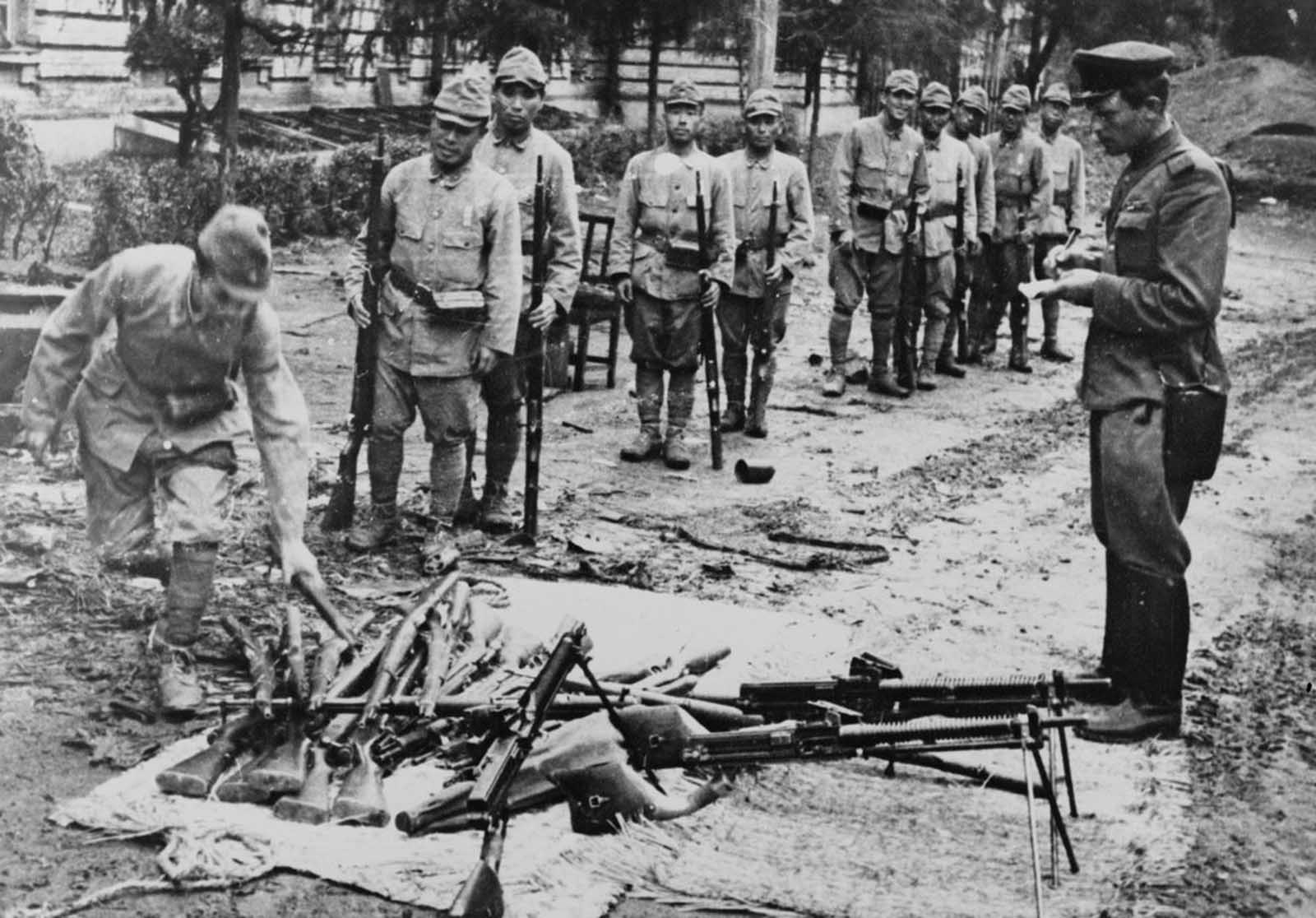 Japanese soldiers surrendering their rifles as a Soviet soldier records information in a book in 1945.
