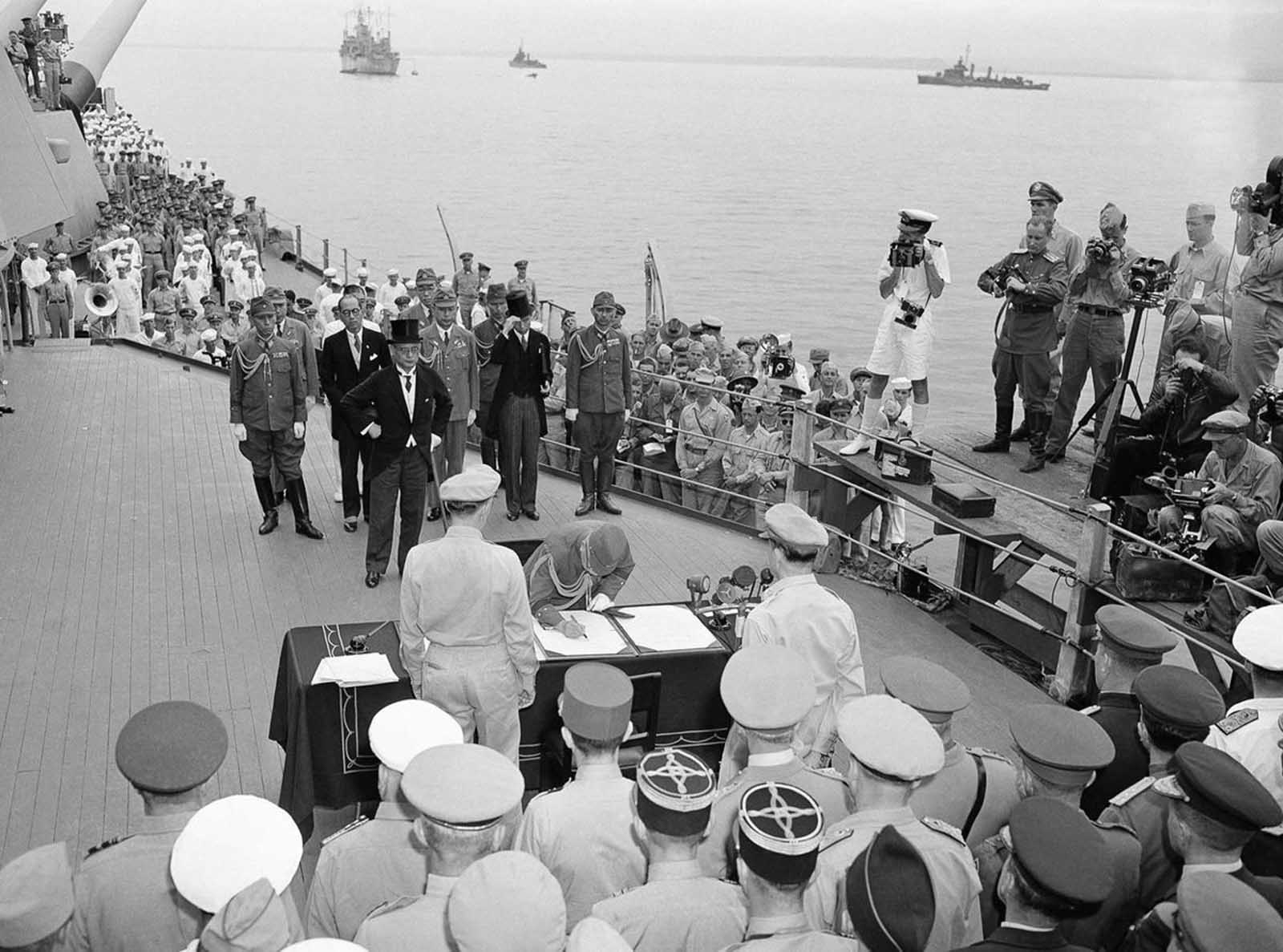 The scene aboard the battleship Missouri as the Japanese surrender documents were signed in Tokyo Bay, on September 2, 1945. Here, General Yoshijiro Umezu signs the Instrument of Surrender on behalf of the Armed Forces of Japan, Foreign Minister Mamoru Shigemitsu (behind him, in top hat) had earlier signed on behalf of the government. Both men were later tried and convicted of war crimes. Umezu died while in prison, Shigemitsu was paroled in 1950, and served in the Japanese government until his death in 1957.