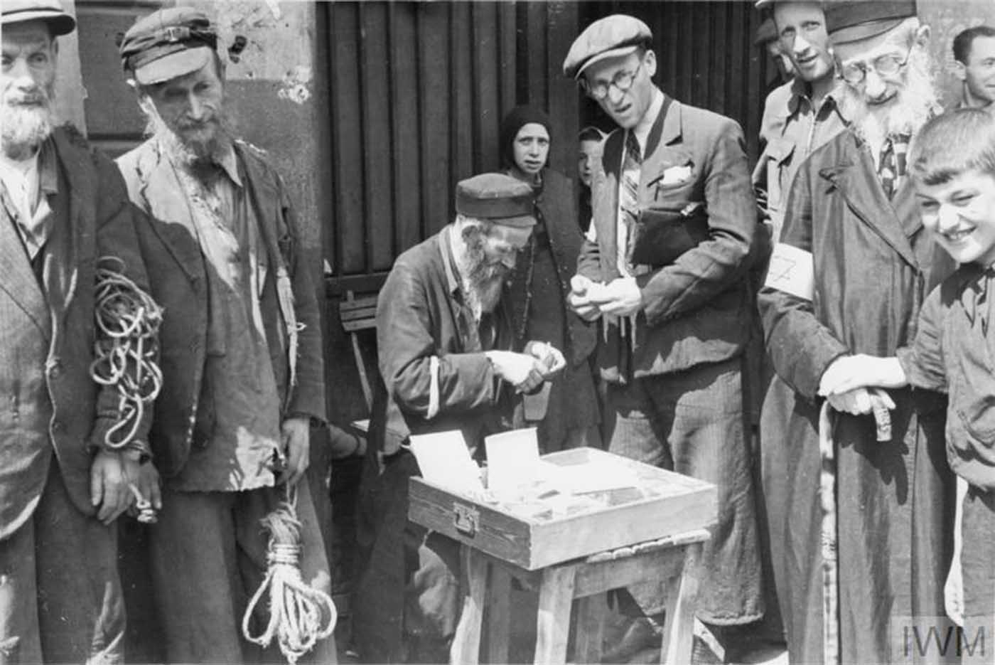 An armband seller making a transaction in the street of the ghetto. Note two elderly Jewish men on the left, probably selling pieces of rope.