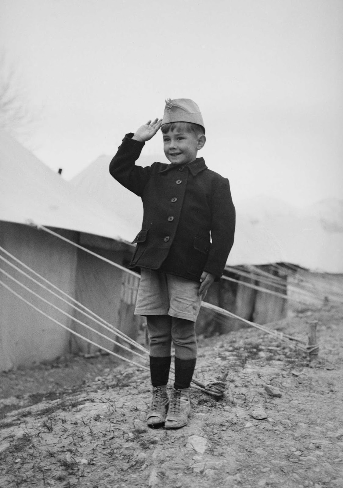 A young Polish refugee does a military salute outside his tent.