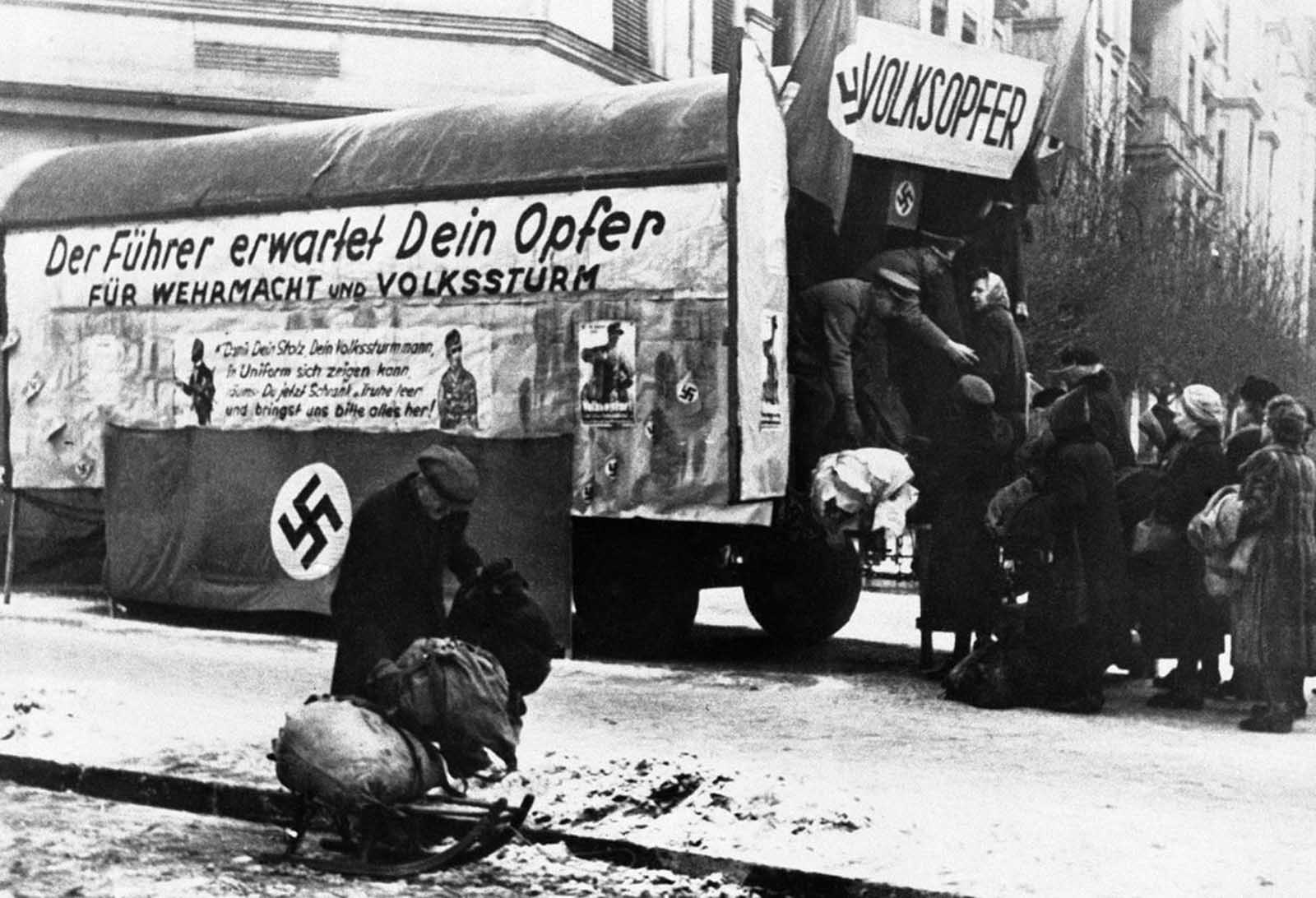 With more and more members of the Volkssturm (Germany's National Militia) being directed to the front line, German authorities were experiencing an ever-increasing strain on their stocks of army equipment and clothing. In a desperate attempt to overcome this deficiency, street to street collection depots called the Volksopfer, meaning Sacrifice of the people, scoured the country, collecting uniforms, boots and equipment from German civilians, as seen here in Berlin on February 12, 1945. The Volksopfer bears the words 