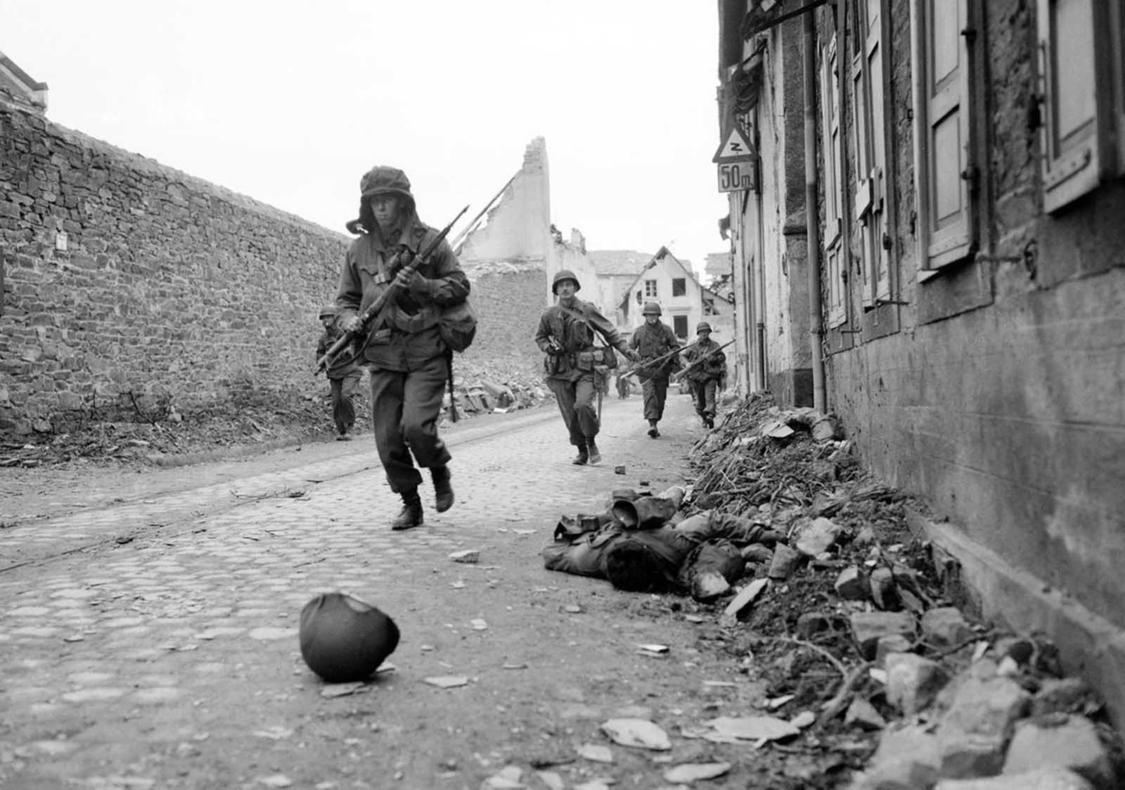 Soldiers of the 3rd U.S. Army storm into Coblenz, Germany, as a dead comrade lies against the wall, on March 18, 1945.