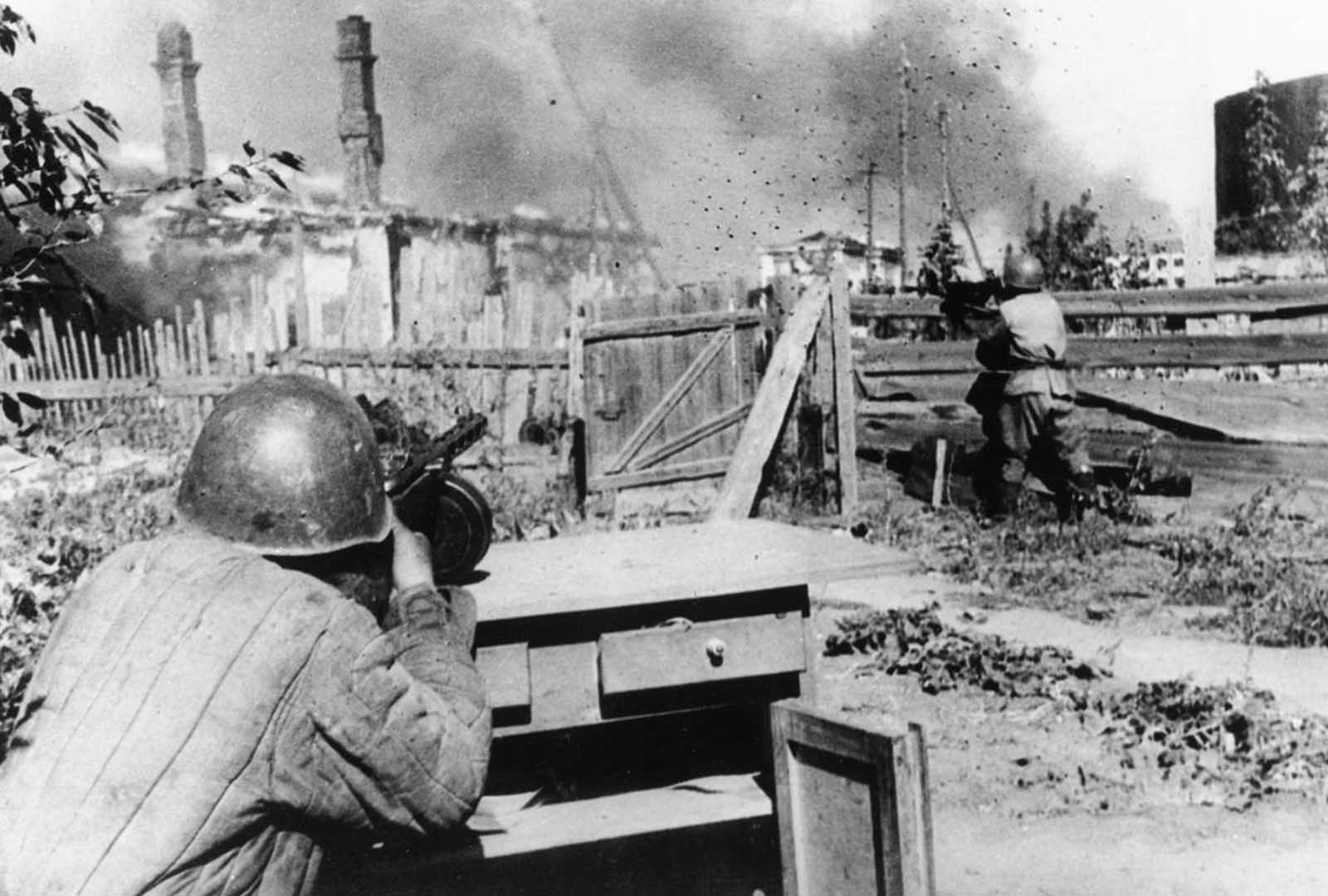 Standing in the backyard of an abandoned house in the outskirts of the besieged city of Leningrad, a rifleman of the Red Army aims and fires his machine gun at German positions on December 16, 1942.