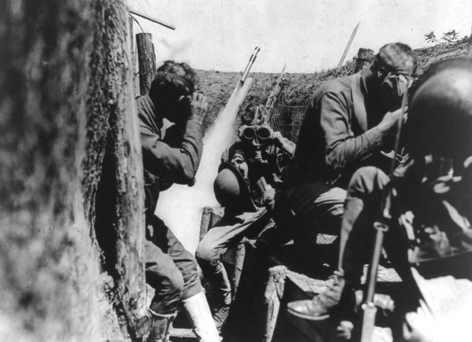 U.S. soldiers in trench putting on gas masks. Behind them, a signal rocket appears to be in mid-launch. When gas attacks were detected, alarms used included gongs and signal rockets.