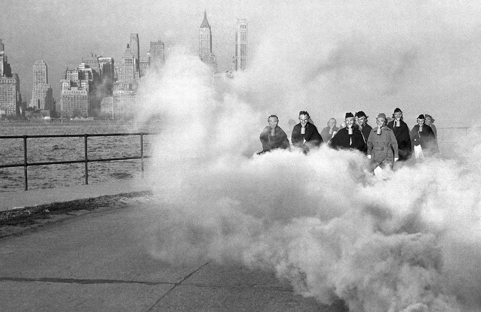 With some of New York's skyscrapers looming through clouds of gas, some U.S. army nurses at the hospital post at Fort Jay, Governors Island, New York, wear gas masks as they drill on defense precautions, on November 27, 1941.