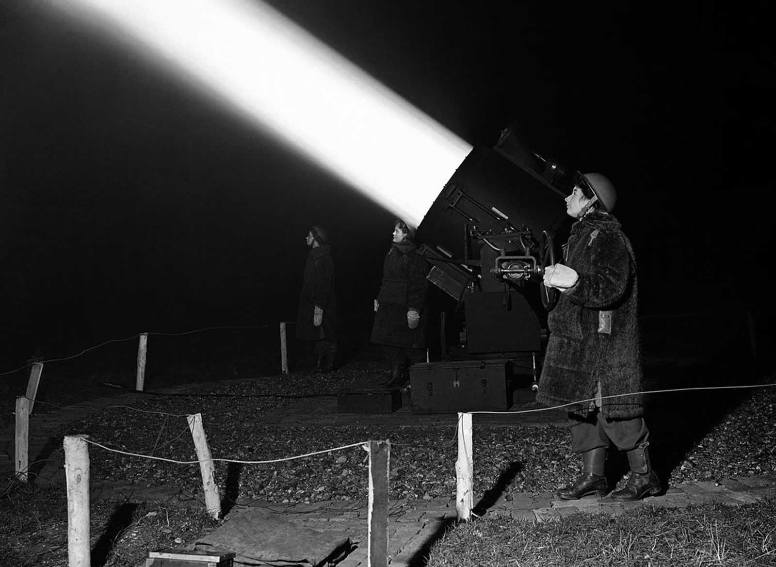 An Auxiliary Territorial Service girl crew, dressed in warm winter coats, works a searchlight near London, on January 19, 1943, trying to find German bombers for the anti-aircraft guns to hit.