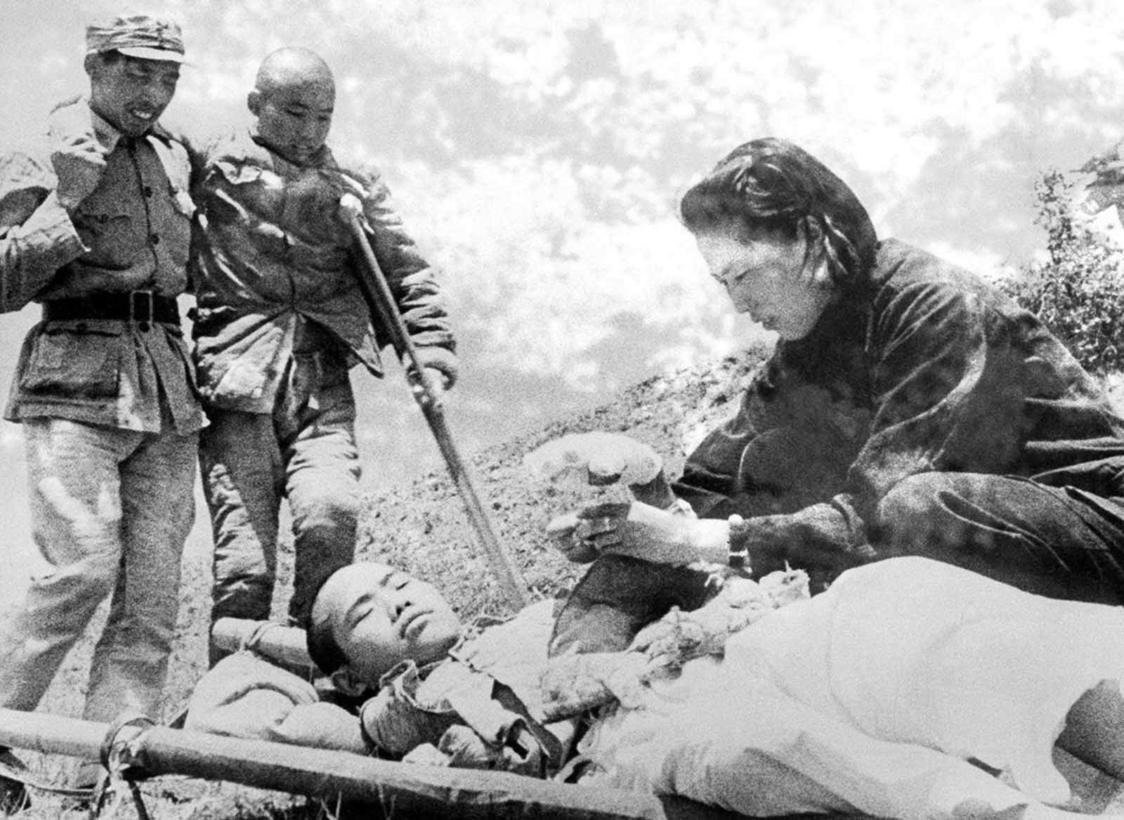 A nurse wraps a bandage around the hand of a Chinese soldier as another wounded soldier limps up for first aid treatment during fighting on the Salween River front in Yunnan Province, China, on June 22, 1943.