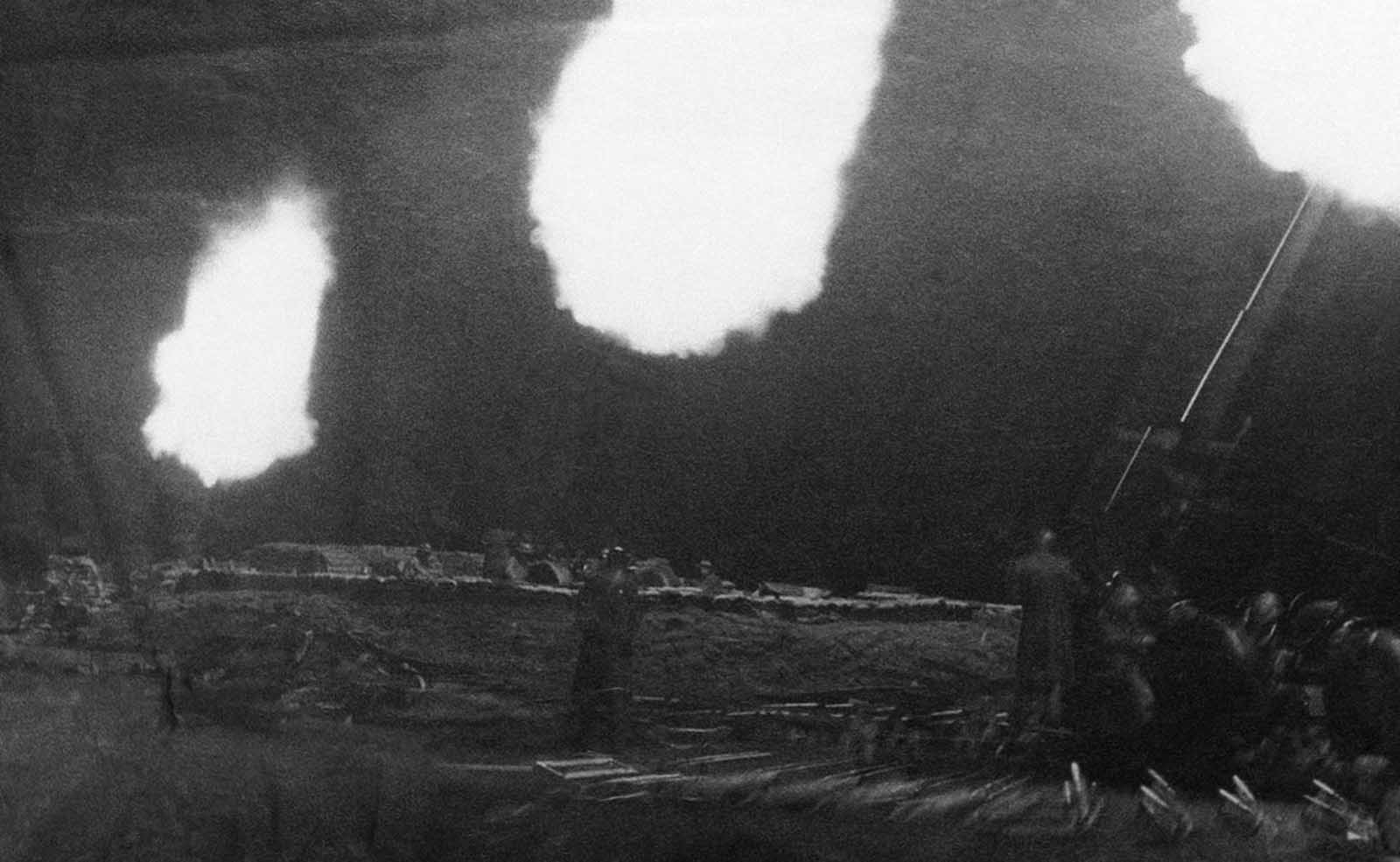 Three anti-aircraft guns flash in the dark in London, on September 20, 1940, throwing shells at raiding German planes. Shells in stacked rows behind the guns leap about as the concussions from the firing loosen them.