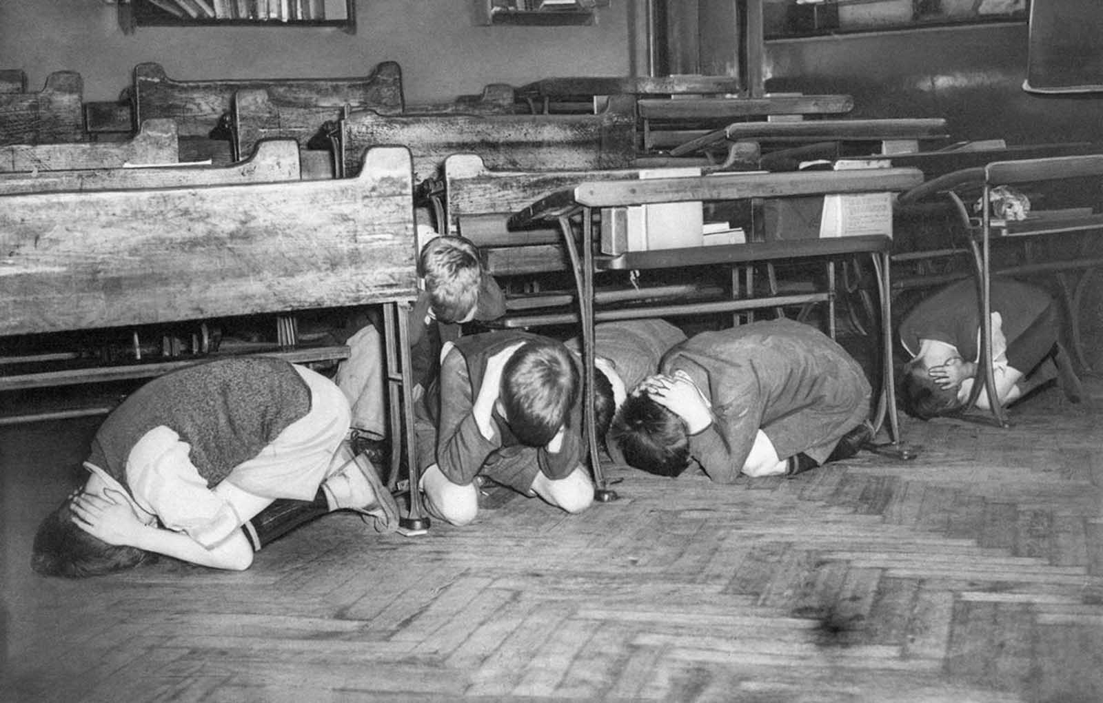 These London schoolchildren are in the midst of an air raid drill ordered by the London Board of Education as a precaution in case an air raid comes too fast to give the youngsters a chance to leave the building for special shelters, on July 20, 1940. They were ordered to go to the middle of the room, away from windows, and hold their hands over the backs of their necks.