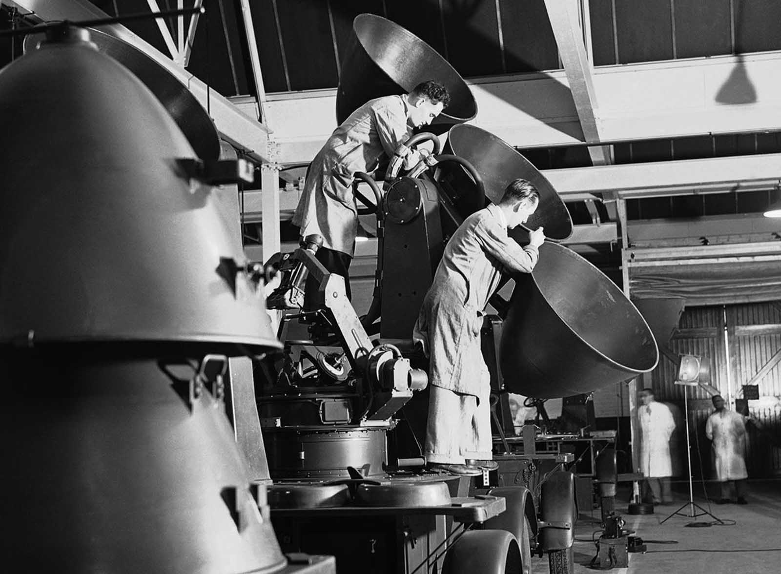 Workmen fit a set of paraboloids in a sound detector for use by anti-aircraft batteries guarding England, in a factory somewhere in England, on July 30, 1940.