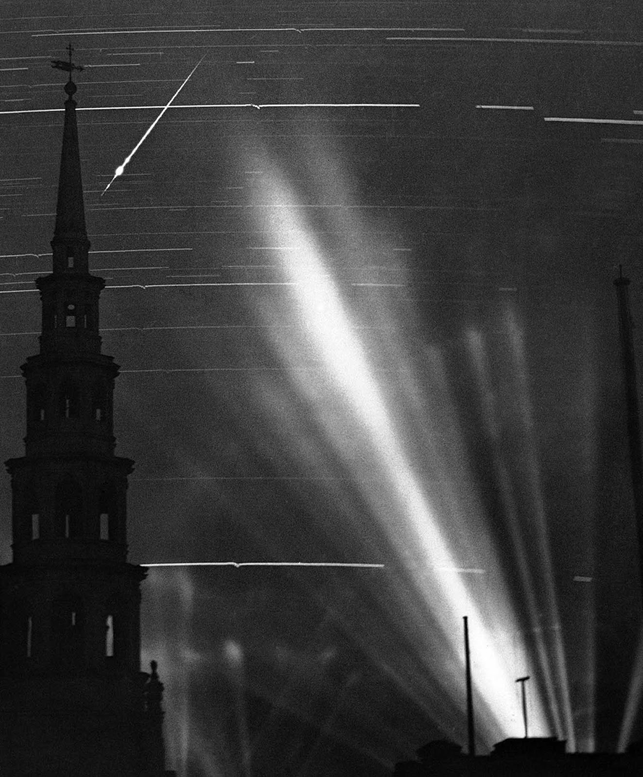 A ninety minute exposure taken from a Fleet Street rooftop during an air raid in London, on September 2, 1940. The searchlight beams on the right had picked up an enemy raider. The horizontal marks across the image are from stars and the small wiggles in them were caused by the concussions of anti-aircraft fire vibrating the camera. The German pilot released a flare, which left a streak across the top left, behind the steeple of St. Bride's Church.