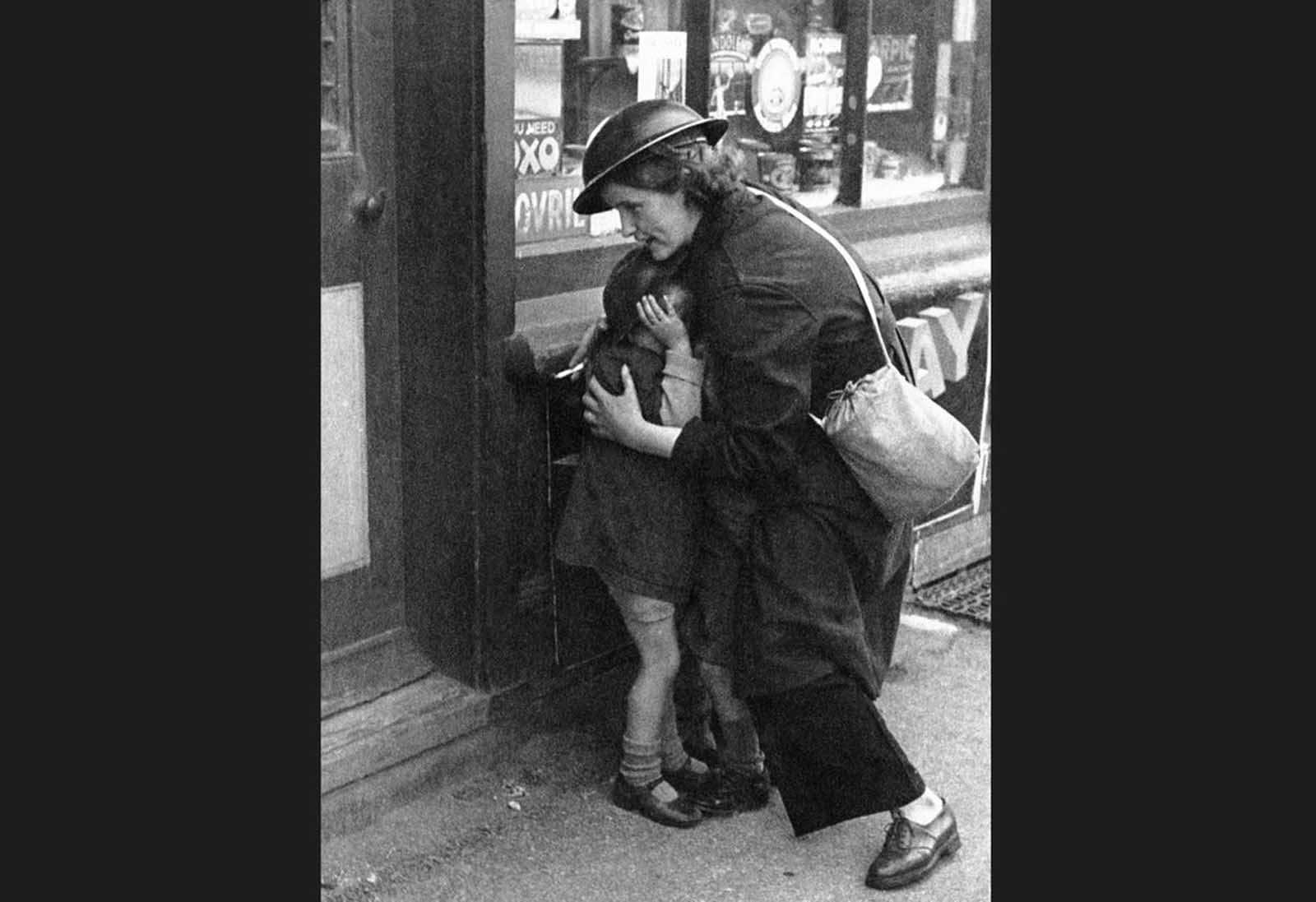 Mrs. Mary Couchman, a 24-year-old warden of a small Kentish Village, shields three little children, among them her son, as bombs fall during an air attack on October 18, 1940. The three children were playing in the street when the siren suddenly sounded. Bombs began to fall as she ran to them and gathered the three in her arms, protecting them with her body. Complimented on her bravery, she said,