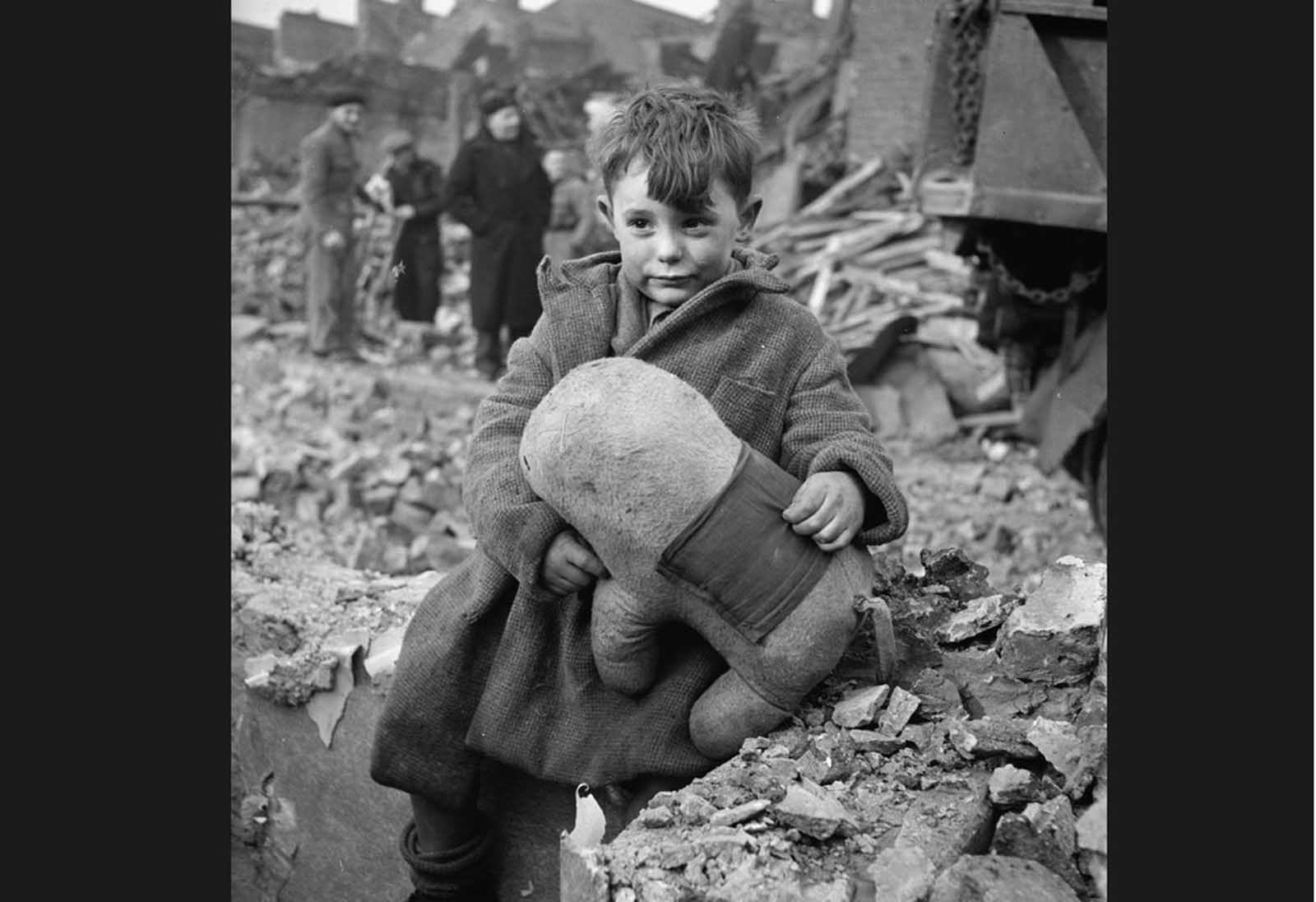 An abandoned boy, holding a stuffed toy animal amid ruins following a German aerial bombing of London in 1940.