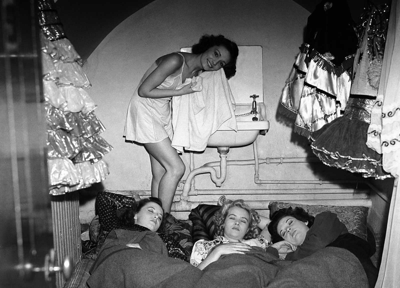 Through bombs and sirens, the Windmill Theatre carried on providing music, revue, and ballet performances for the people of wartime London. The artists sleep on mattresses in their dressing rooms, living and eating on the premises. Here, a scene behind the scenes shows one of the girls having a wash while the others sleep soundly surrounded by their picturesque costumes, after the show on September 24, 1940, in London.