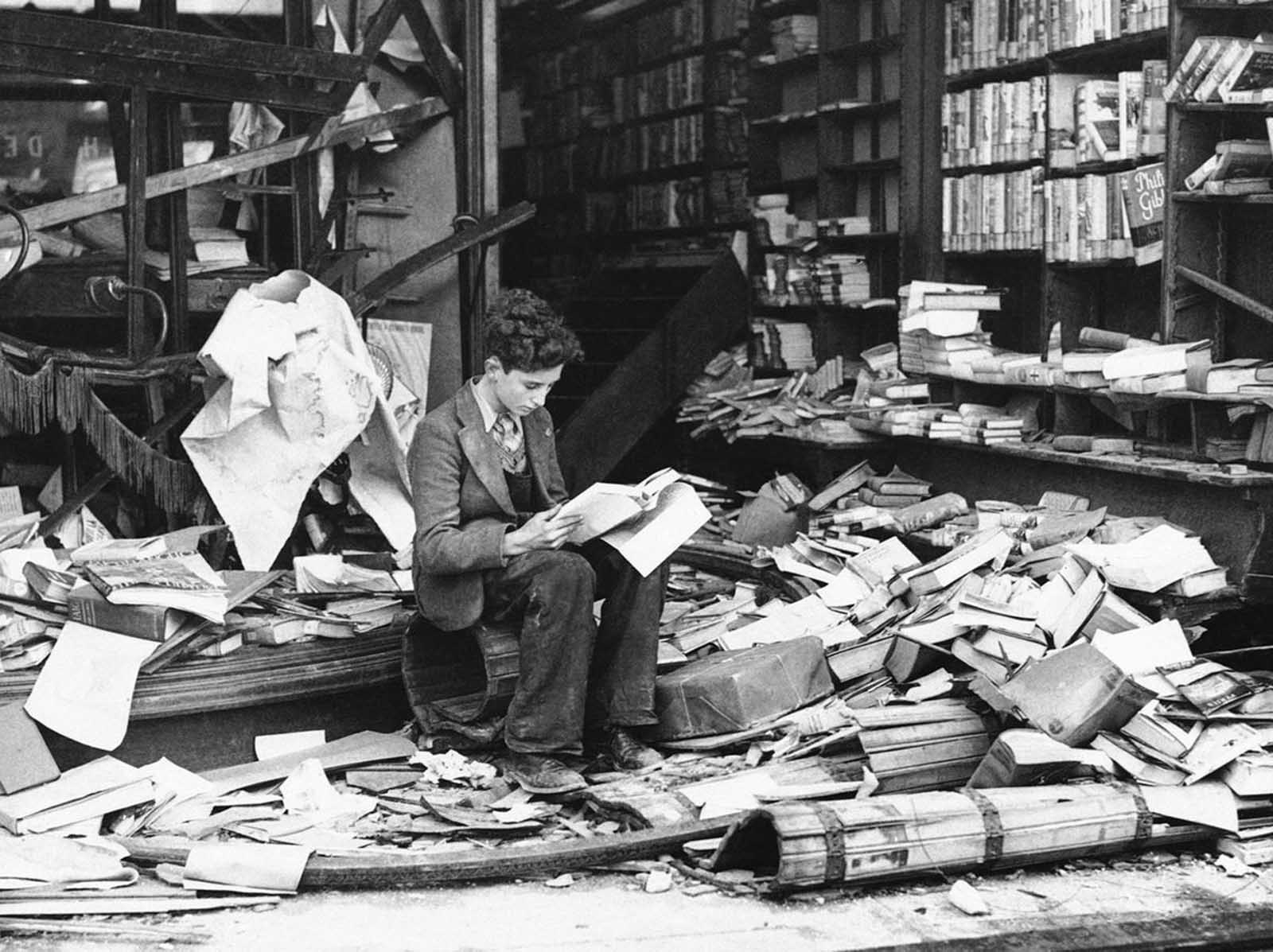 A boy sits amid the ruins of a London bookshop following an air raid on October 8, 1940, reading a book titled