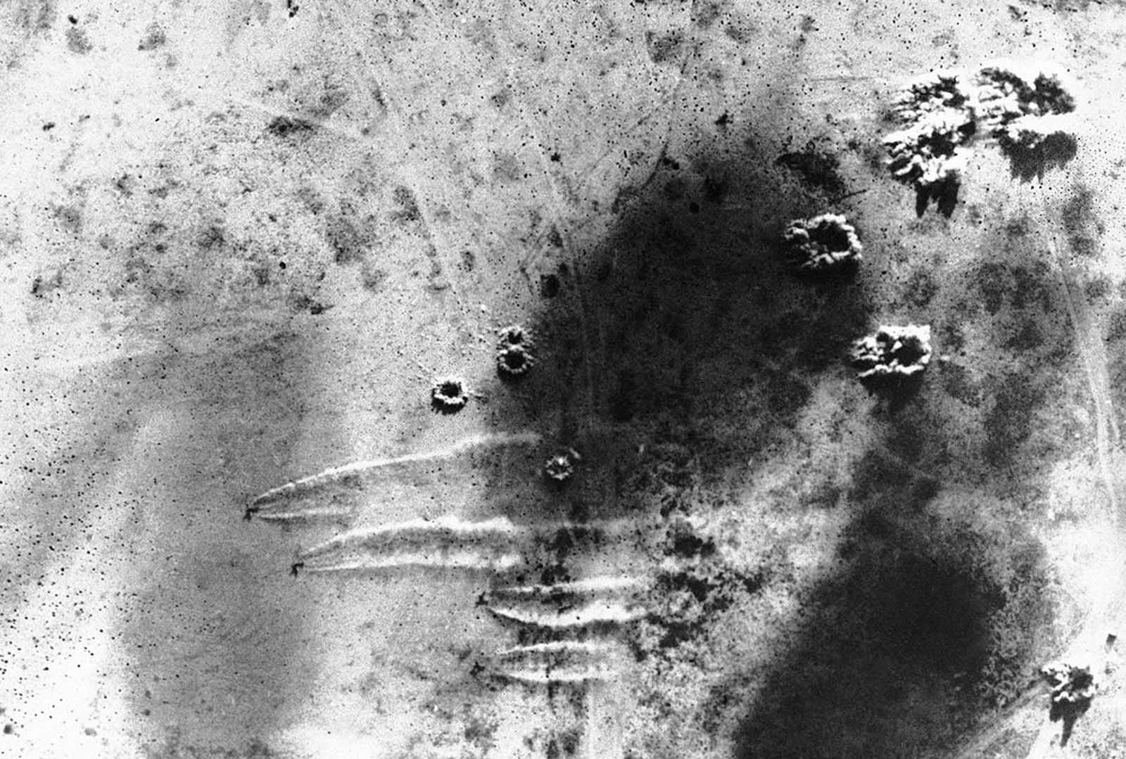 This view of an air raid on an Axis plane base at Martuba, near Derna, in Libya on July 6, 1942 was made from one of the South African planes which took part in the raid. The four sets of white streaks in the lower half show the dust of Axis planes speeding along the ground to escape as bomb bursts appear near them and in upper center.