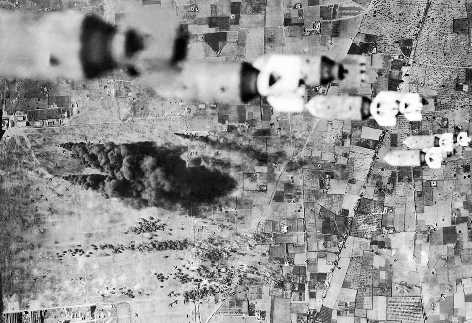 B-17 bombers, of the U.S. Army's Twelfth Air force, dropped fragmentation bombs on the important El Aouina airdrome at Tunis, Tunisia, and covered the airdrome and field completely. On the field below enemy planes can be seen burning, on February 14, 1943.