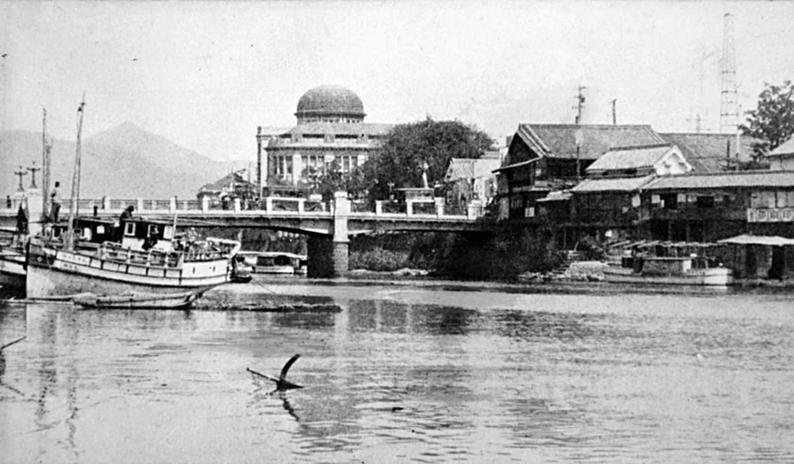 Looking upstream on the Motoyasugawa, toward the Product Exhibition Hall building (dome) in Hiroshima, before the bombing. The domed building was almost directly below the detonation, which occurred in mid-air, about 2,000 feet (600 meters) above this spot. Today, much of the building remains standing, and is known as the Atomic Bomb Dome, or the Hiroshima Peace Memorial.