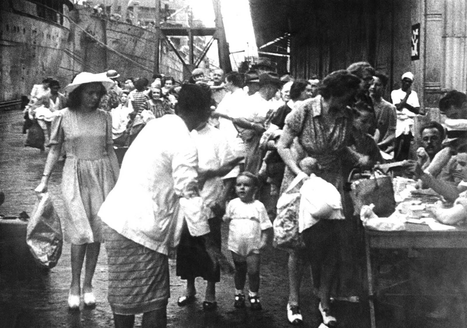 In Singapore, women and children were evacuated from the onetime British bastion before the Japanese invasion. Here, some of the women, carrying bags and paper sacks, register before boarding a waiting ship on March 9, 1942.