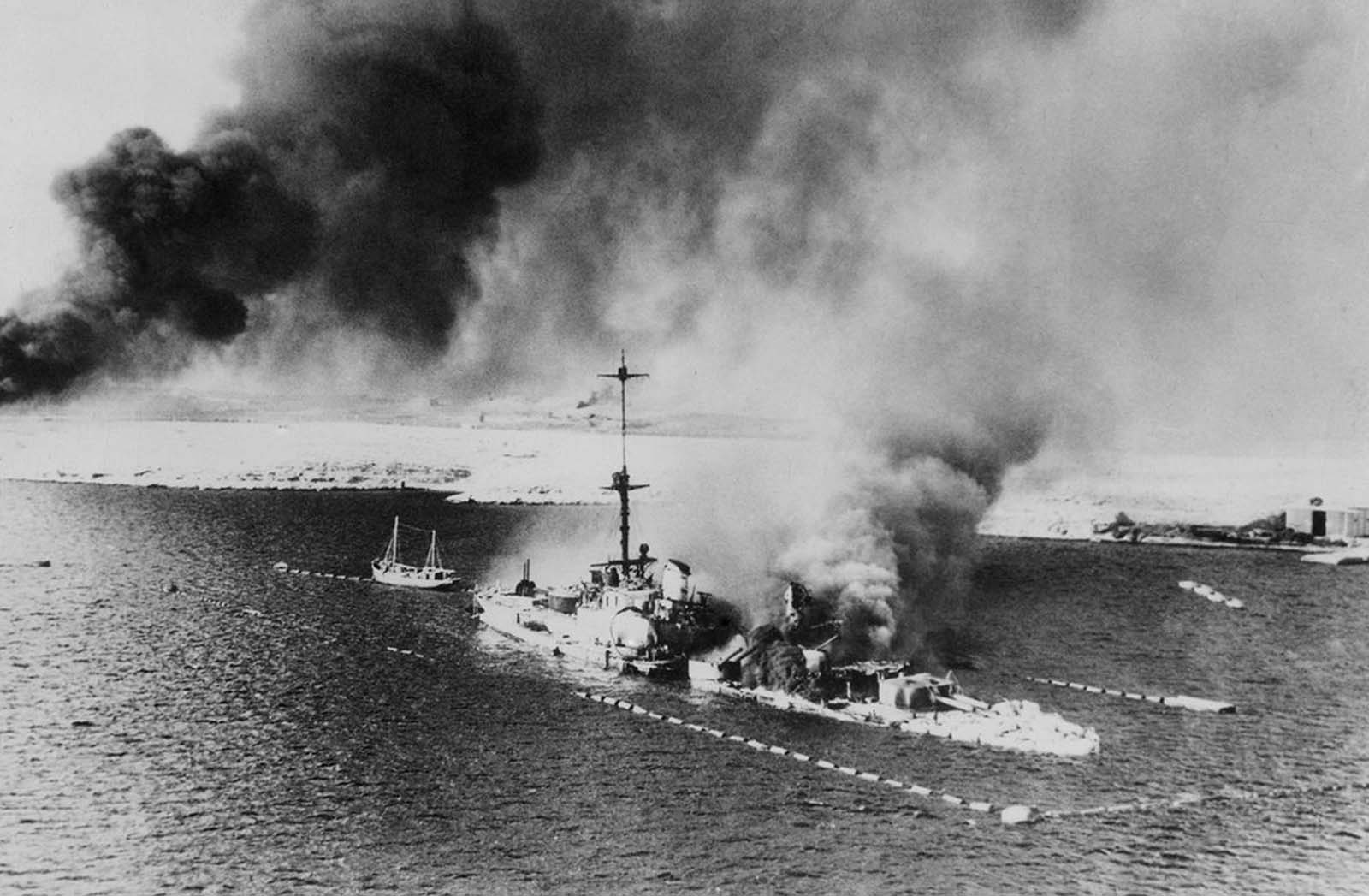 This photo, made from a British warplane during the assault of Tobruk shows the Italian Cruiser San Giorgio, burning amidships, in the harbor of Tobruk, on February 18, 1941. The ship was scuttled, its decks appear to be covered with wrecked and smashed gear.