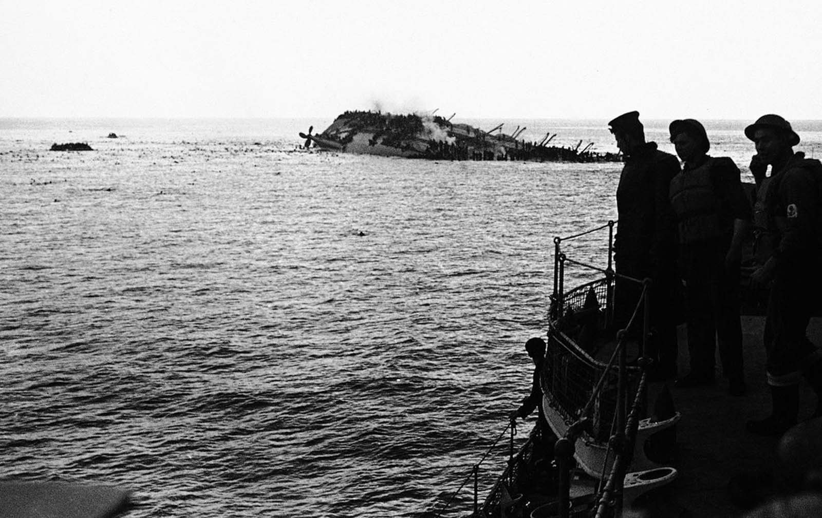 The dramatic and tragic scene as the Cunard White Star liner Lancastria was sunk on August 3, 1940. The Lancastria was evacuating British nationals and troops from France, and had boarded as many as possible for the short trip - an estimated 4,000 to 9,000 passengers were aboard. A German Junkers 88 aircraft bombed the ship shortly after it departed, and it sank within twenty minutes. While 2,477 were rescued, an estimated 4,000 others perished by bomb blasts, strafing, drowning, or choking in oil-fouled water. Photo taken from one of the rescue boats as the liner heels over, as men swarm down her sides and swim for safety to the rescue ships. Note the large number of bobbing heads in the water.