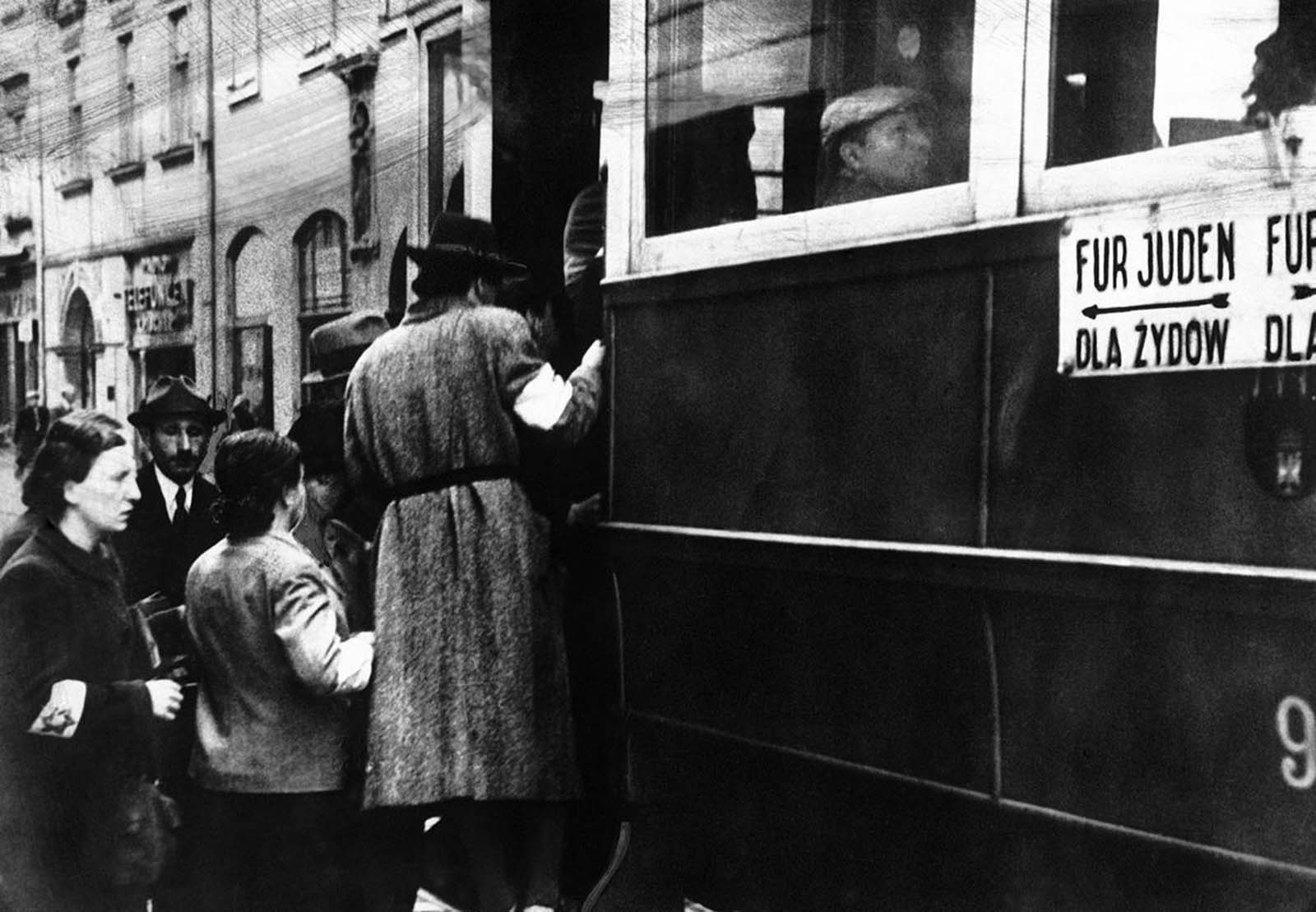 A scene from the Warsaw Ghetto where Jews are seen wearing white armlets bearing the Star of David and trams are seen marked with the words