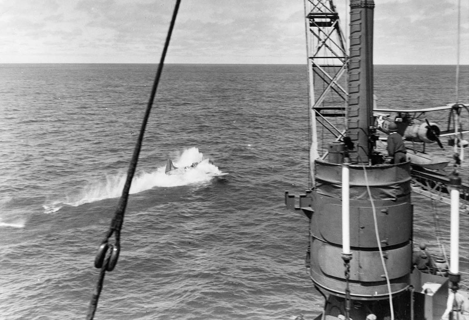 U.S. Navy LCdr Maxwell F. Leslie, commanding officer of bombing squadron VB-3, ditches in the ocean next to the heavy cruiser USS Astoria, after successfully attacking the Japanese carrier Soryu during the Battle of Midway, on June 4, 1942. Leslie and his wingman Lt(jg) P.A. Holmberg ditched near Astoria due to fuel exhaustion, after their parent carrier USS Yorktown was under attack by Japanese planes when they returned. Leslie, Holmberg, and their gunners were rescued by one of the cruiser's whaleboats. Note one of the cruiser's Curtiss SOC Seagull floatplanes on the catapult at right.