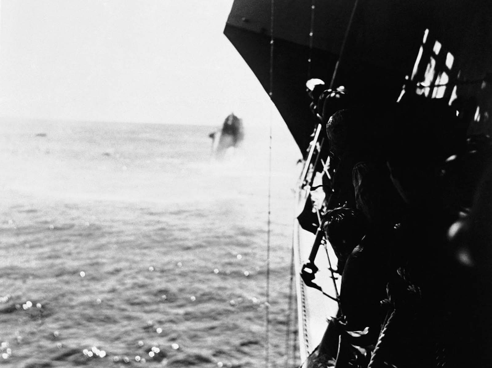 The United States destroyer Hammann, background, on its way to the bottom of the Pacific after having been hit by a Japanese torpedo during the battle of Midway, in June of 1942. The Hammann had been providing auxiliary power to damaged USS Yorktown while salvage operations were underway. The same attack also struck the Yorktown, which sank the following morning. Crewmen of another U.S. warship, foreground, line the rail as their vessel stands by to rescue survivors.