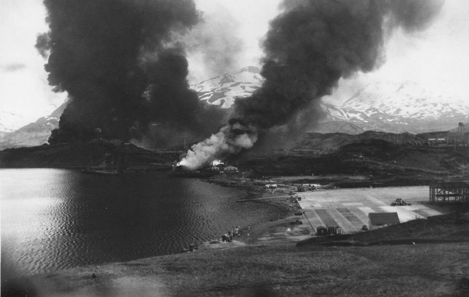 Oil tanks, the SS Northwestern, a beached transport ship, and warehouses on fire after Japanese air raids in Dutch Harbor, Alaska, on June 4, 1942.