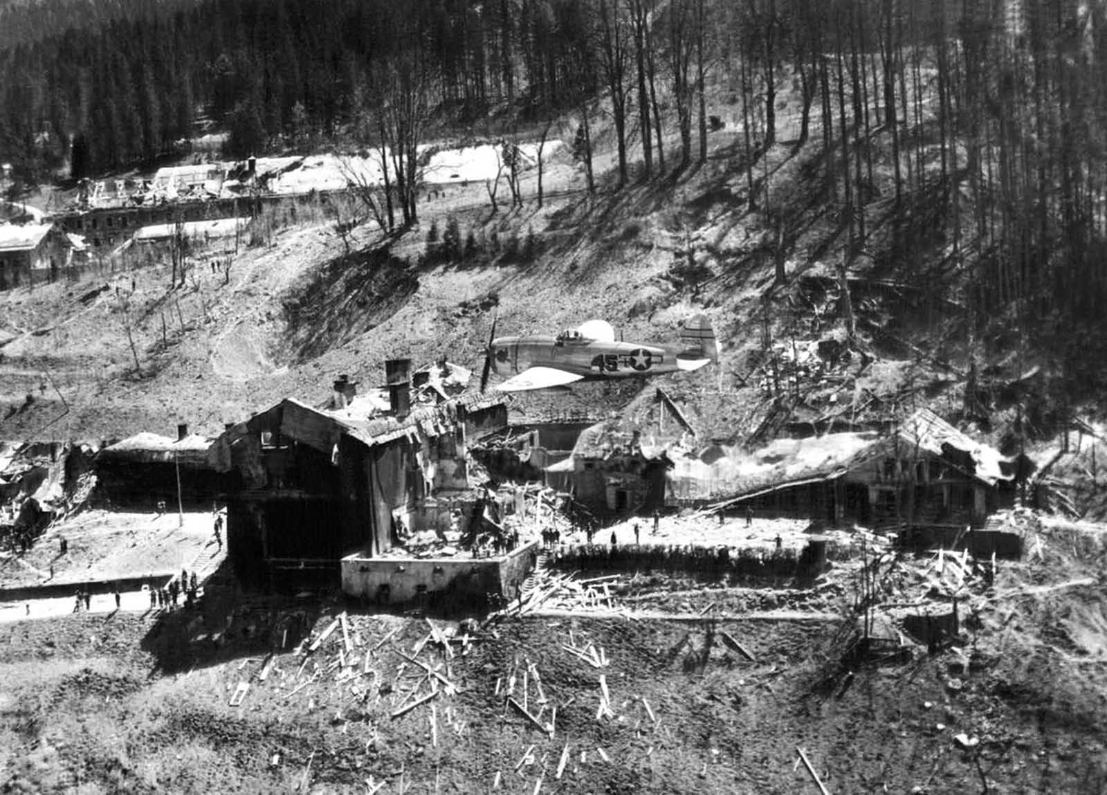 A P-47 Thunderbolt of the U.S. Army 12th Air Force flies low over the crumbled ruins of what once was Hitler's retreat at Berchtesgaden, Germany, on May 26, 1945. Small and large bomb craters dot the grounds around the wreckage.