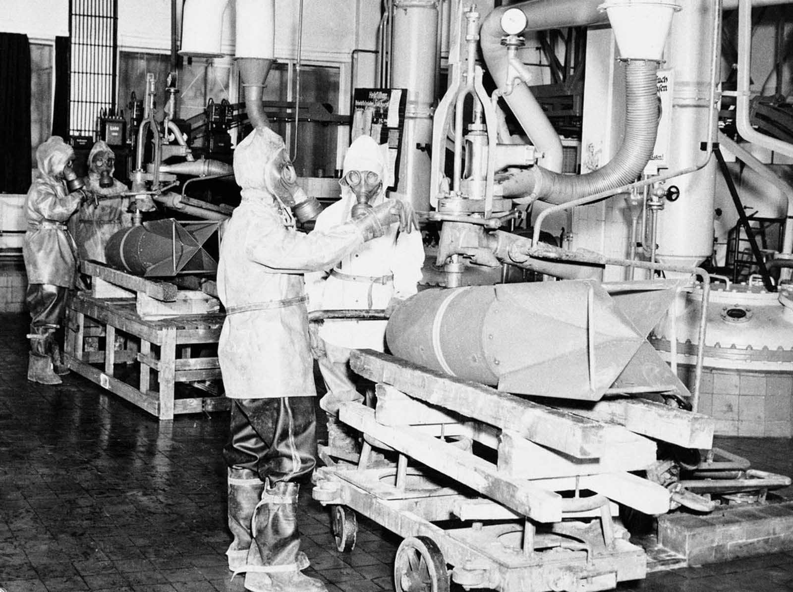 These unidentified German workers in Decontamination clothing destroy toxic bombs on June 28, 1946, at the U.S. Army Chemical Warfare Service Depot, at St. Georgen, Germany. The destruction and disposal of 65,000 dead weight tons of German toxics, including mustard gas, was accomplished in one of two ways: Burning or dumping the empty shells and bombs into the North Sea.