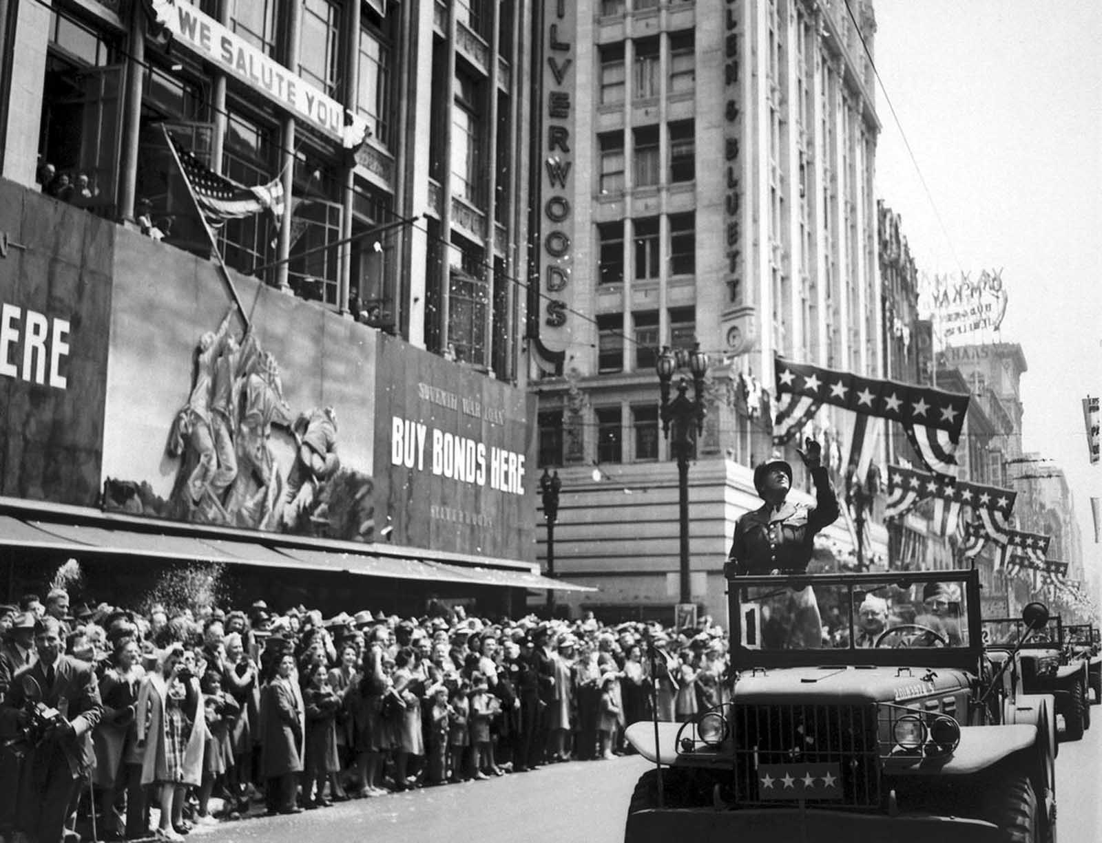U.S. General George S. Patton acknowledges the cheers of thousands during a parade through downtown Los Angeles, California, on June 9, 1945. Shortly thereafter, Patton returned to Germany and controversy, as he advocated the employment of ex-Nazis in administrative positions in Bavaria; he was relieved of command of the 3rd Army and died of injuries from a traffic accident in December, after his return home. Joe Rosenthal's famous Iwo Jima flag-raising photograph is visible on the war bonds billboard.