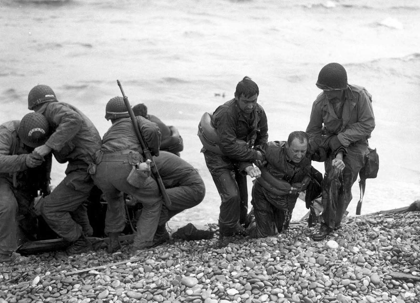 Members of an American landing party help others whose landing craft was sunk by enemy action of the coast of France. These survivors reached Omaha Beach by using a life raft on June 6, 1944.