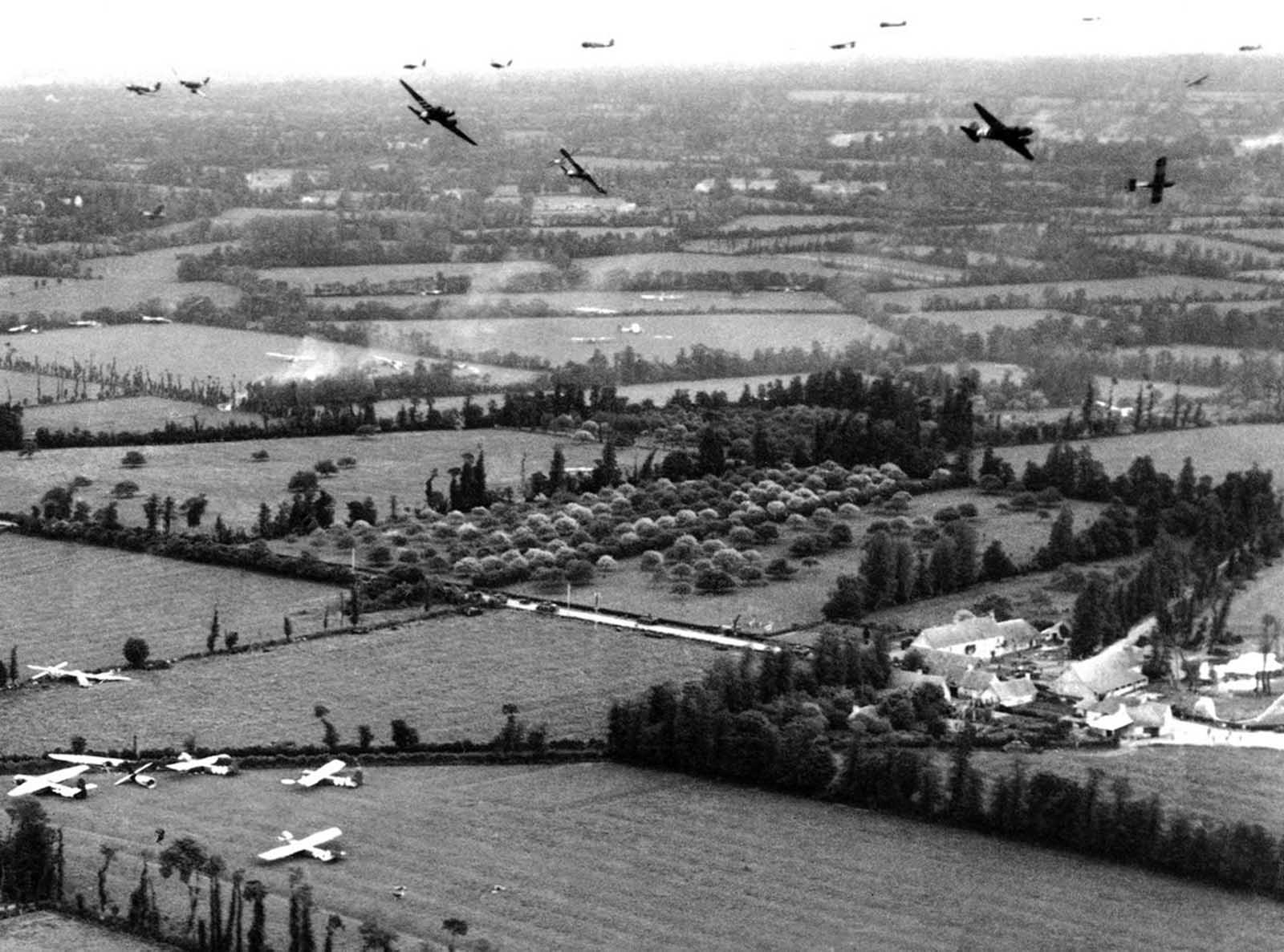 Tow planes and gliders above the French countryside during the Normandy invasion in June of 1944, at an objective of the U.S. Army Ninth Air Force. Gliders and two planes are circling and many gliders have landed in fields below.