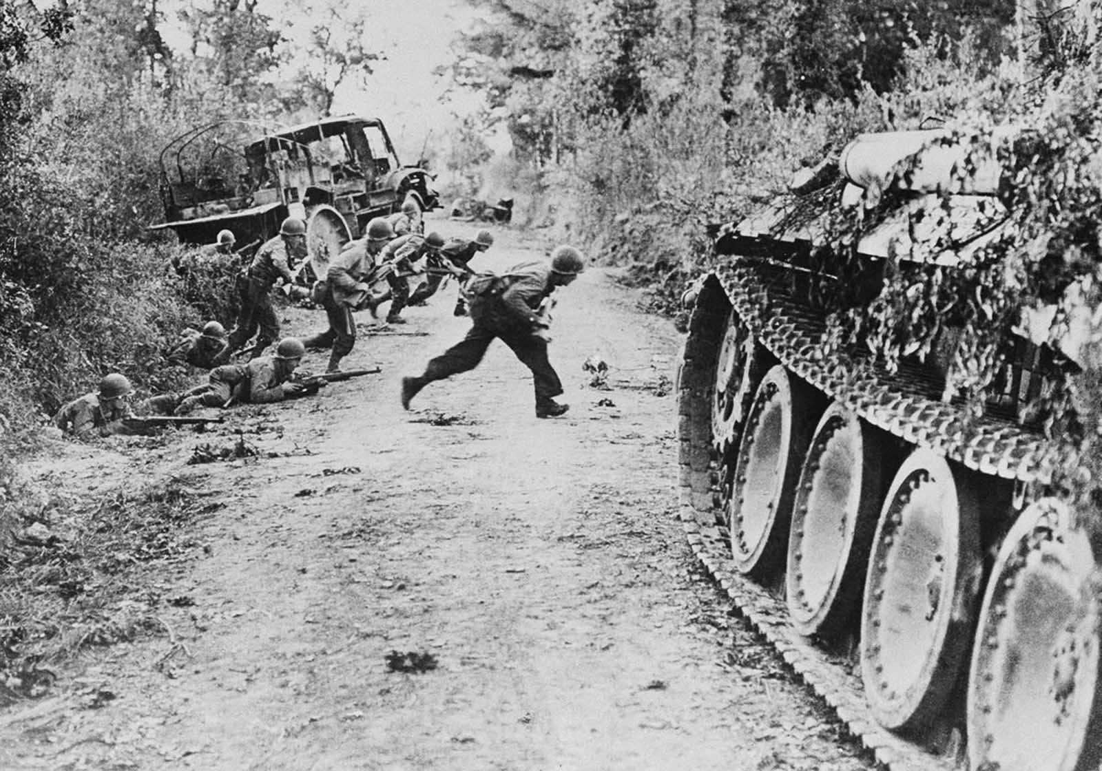 American soldiers race across a dirt road, which is under enemy fire, near St. Lo, in Normandy, France, on July 25, 1944. Others crouch in the ditch before making the crossing.