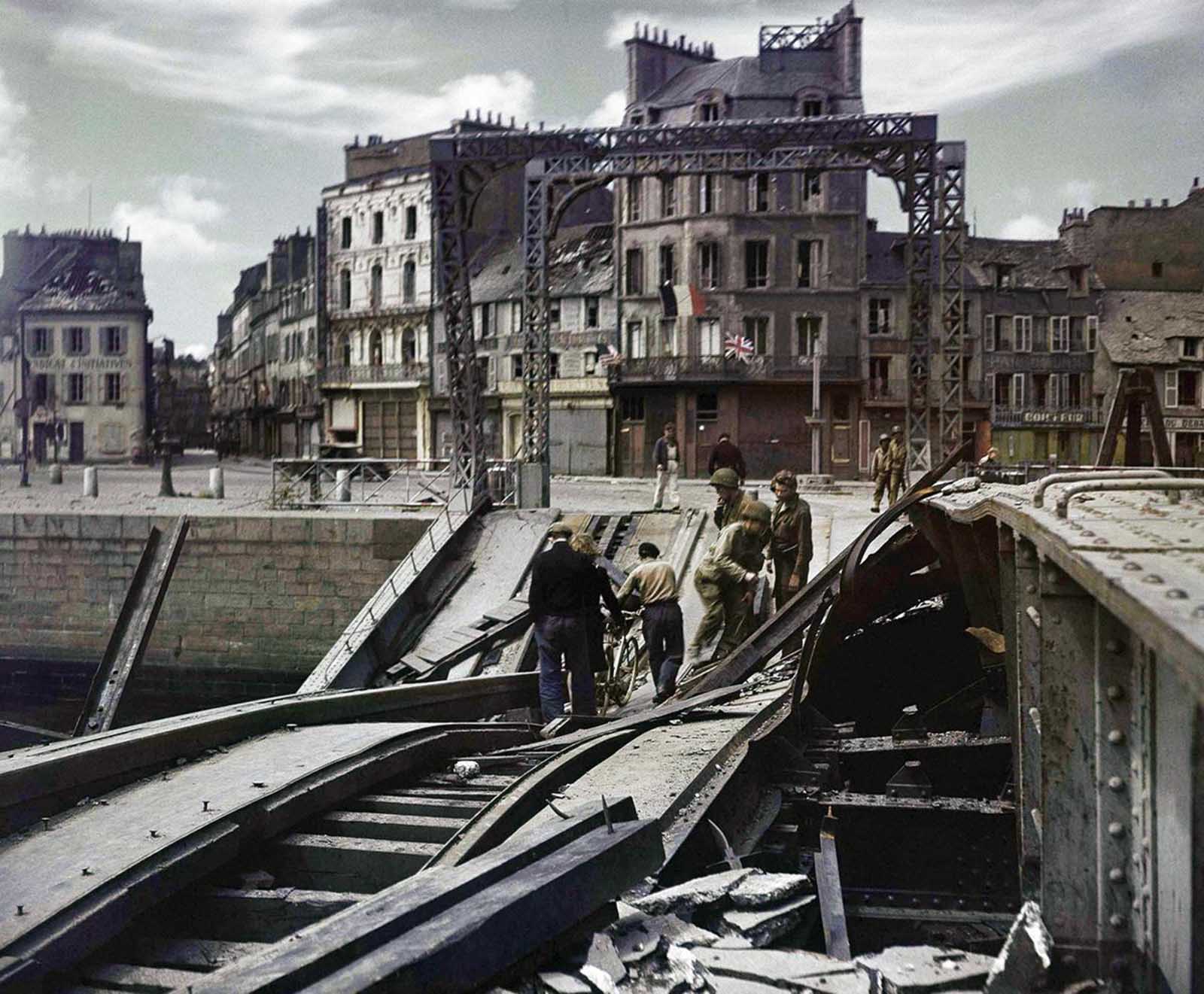 People try to cross a damaged bridge in Cherbourg, France on July 27, 1944.