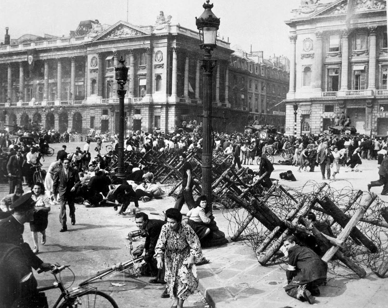 Crowds of Parisians celebrating the entry of Allied troops into Paris scatter for cover as a sniper fires from a building on the place De La Concorde. Although the Germans surrendered the city, small bands of snipers still remained. August 26, 1944.