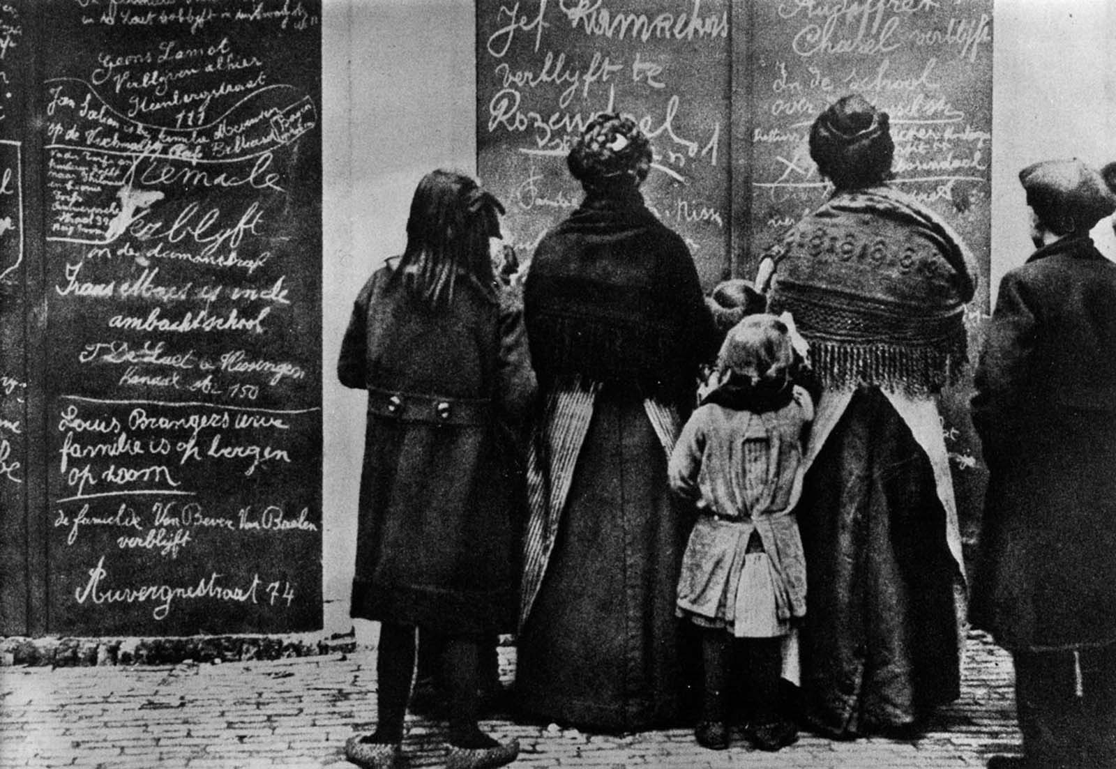 Belgian refugees read Flemish messages left by other refugees in a French town. 1915.