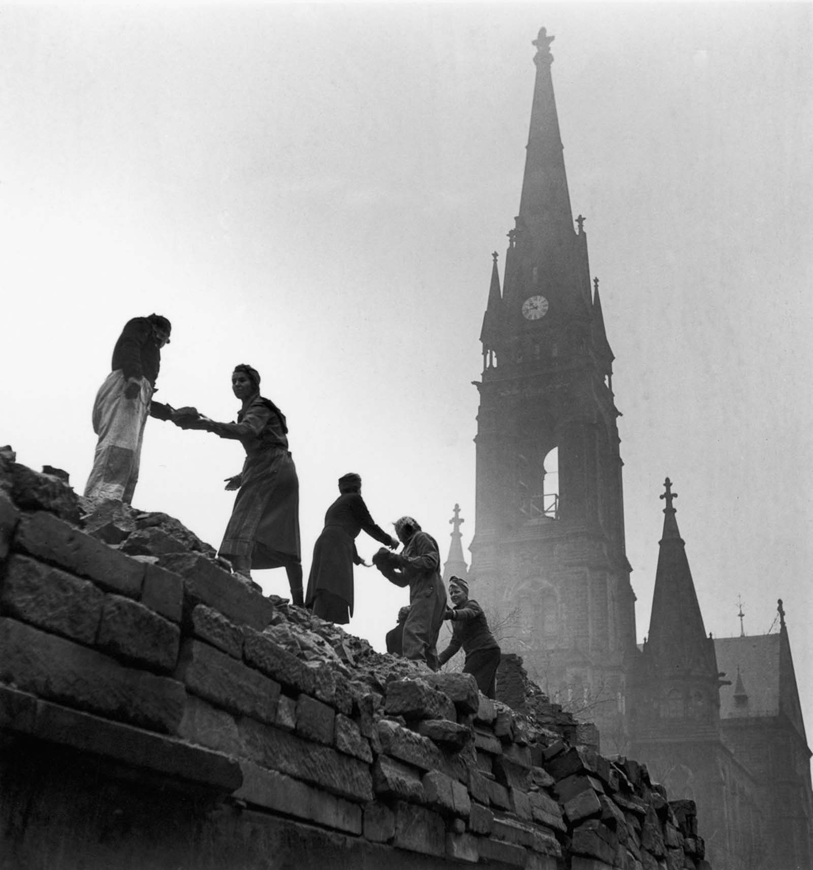 Women pass bricks atop a ruined building. 1946.