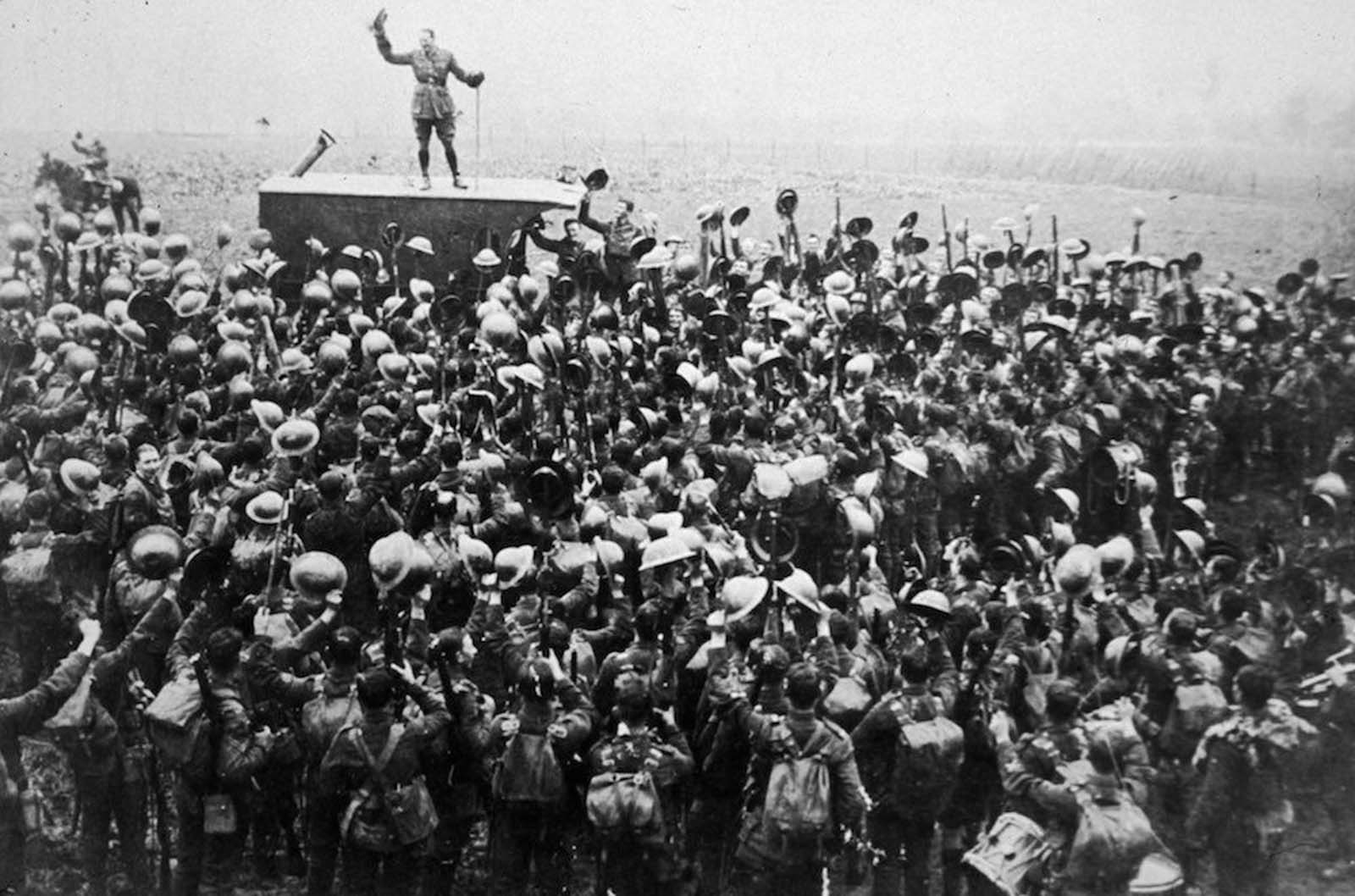 A crowd of soldiers on the Western Front celebrating as an officer announces the news of the Armistice.
