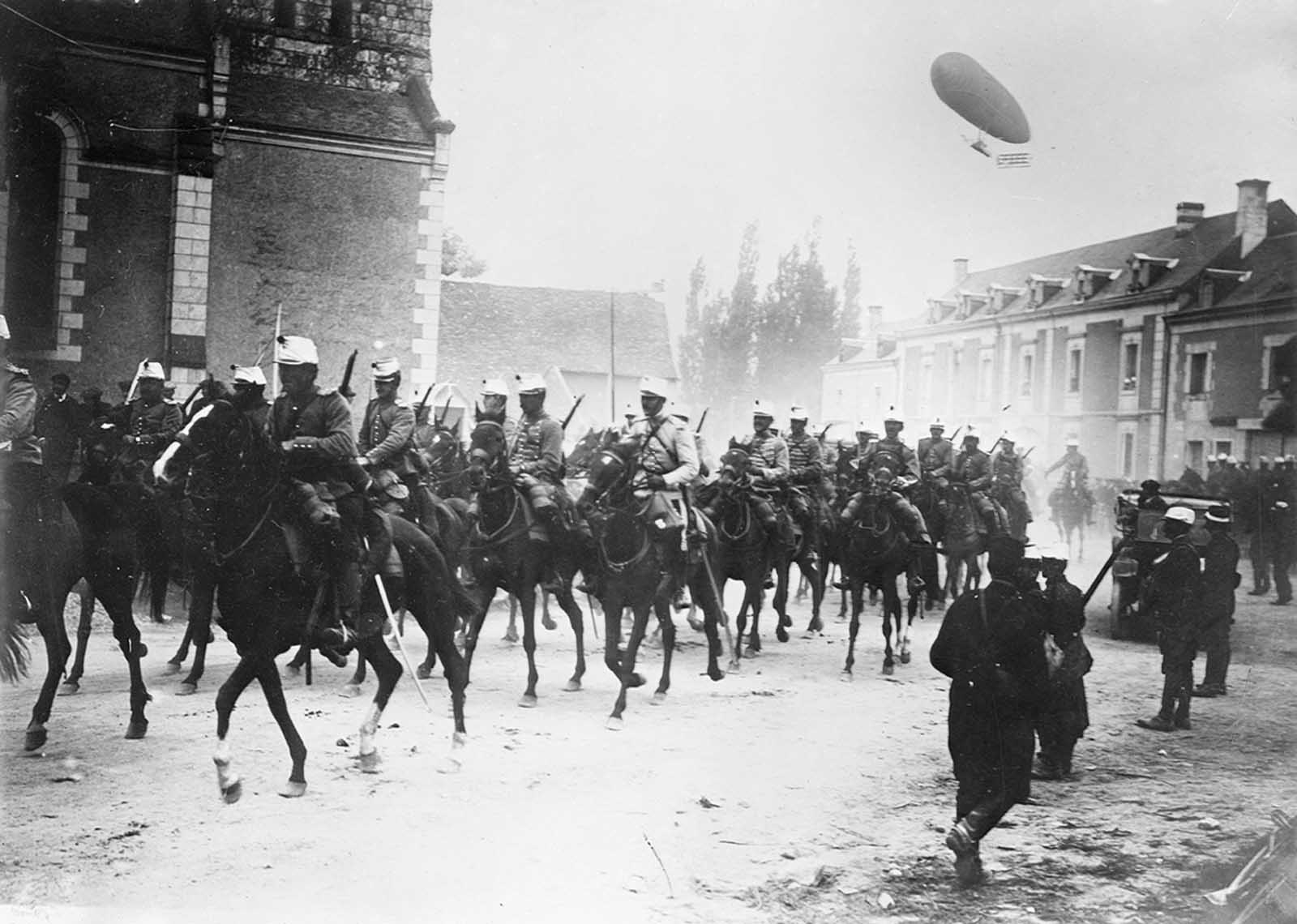 French soldiers on horseback in street, with an airship